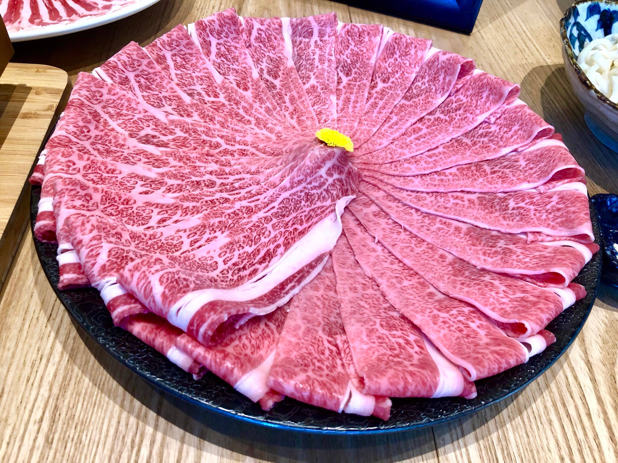 meat 桌布 壁紙 — 一個黑色盤子盛載著薄切雪花牛肉，在木桌上排列成扇形。