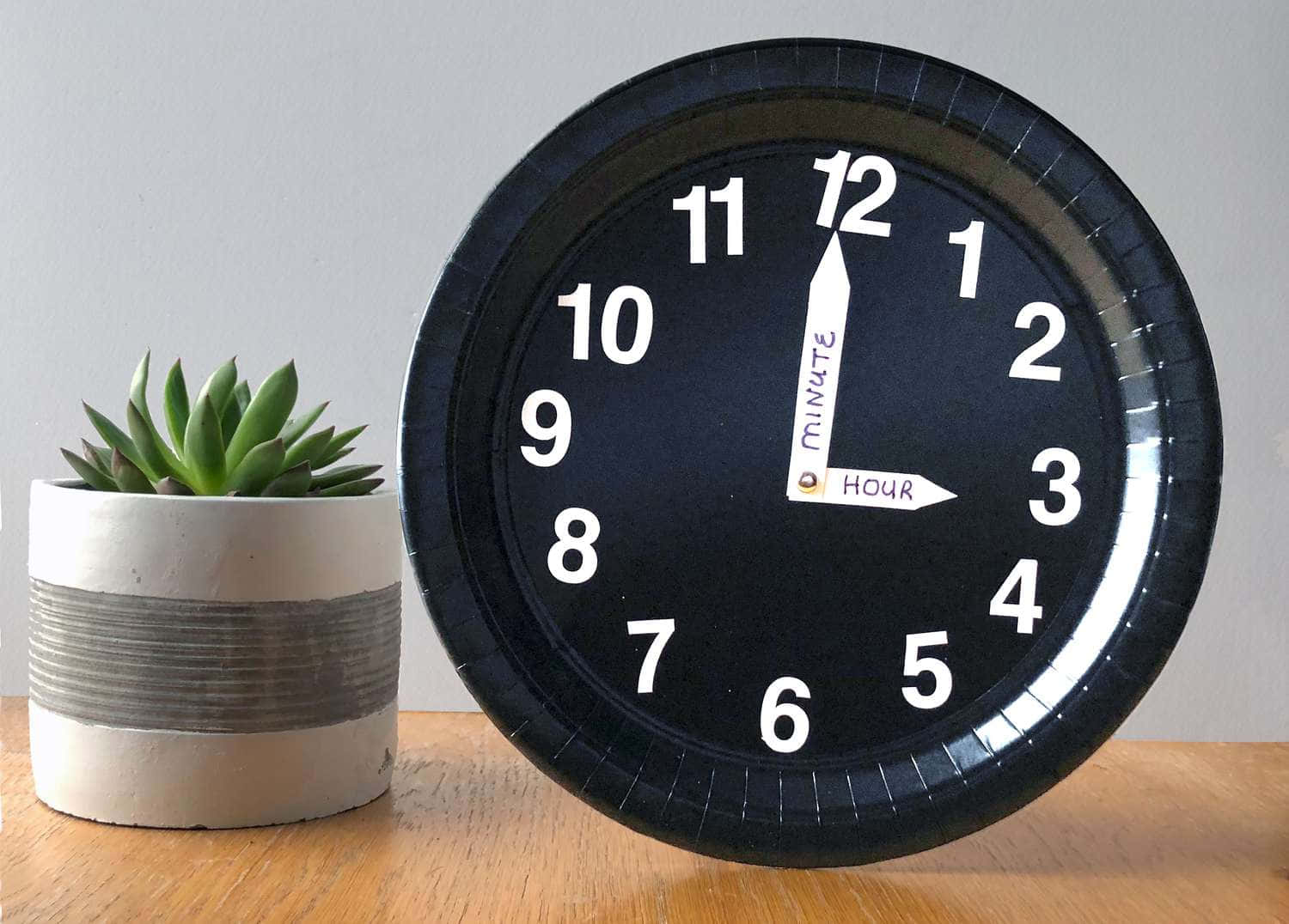 Clocks 桌布 壁紙 — 一個黑色紙盤時鐘，帶有白色數字和指針，放在木桌上的一盆多肉植物旁邊。