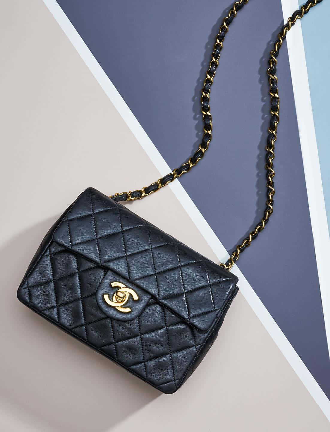 Chanel 桌布 壁紙 — 一個黑色絎縫Chanel手袋搭配金色鏈條肩帶，放置在幾何粉彩背景上。