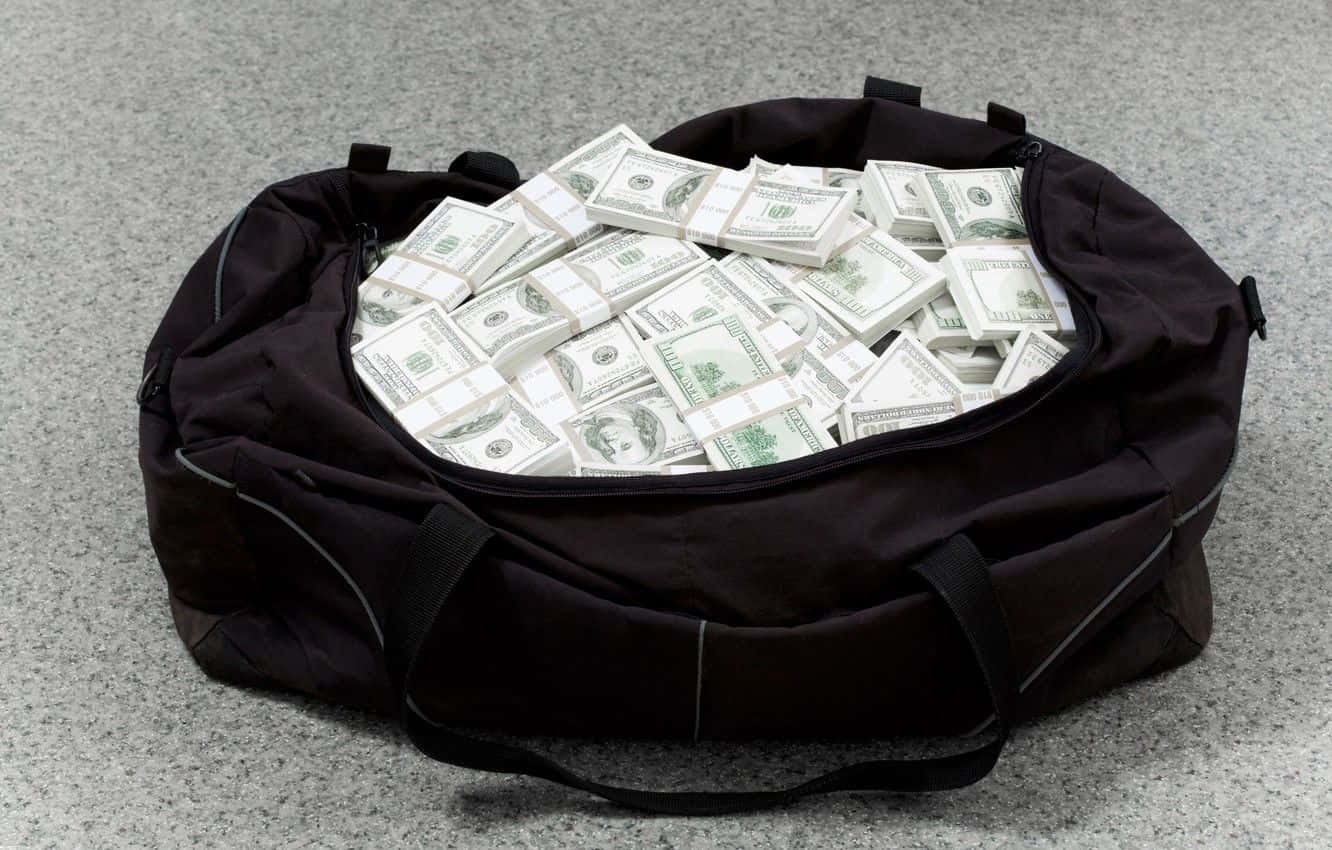 dollar 桌布 壁紙 — 一個黑色行李袋，裡面裝滿了整齊疊放的美鈔，放在灰色地毯上。