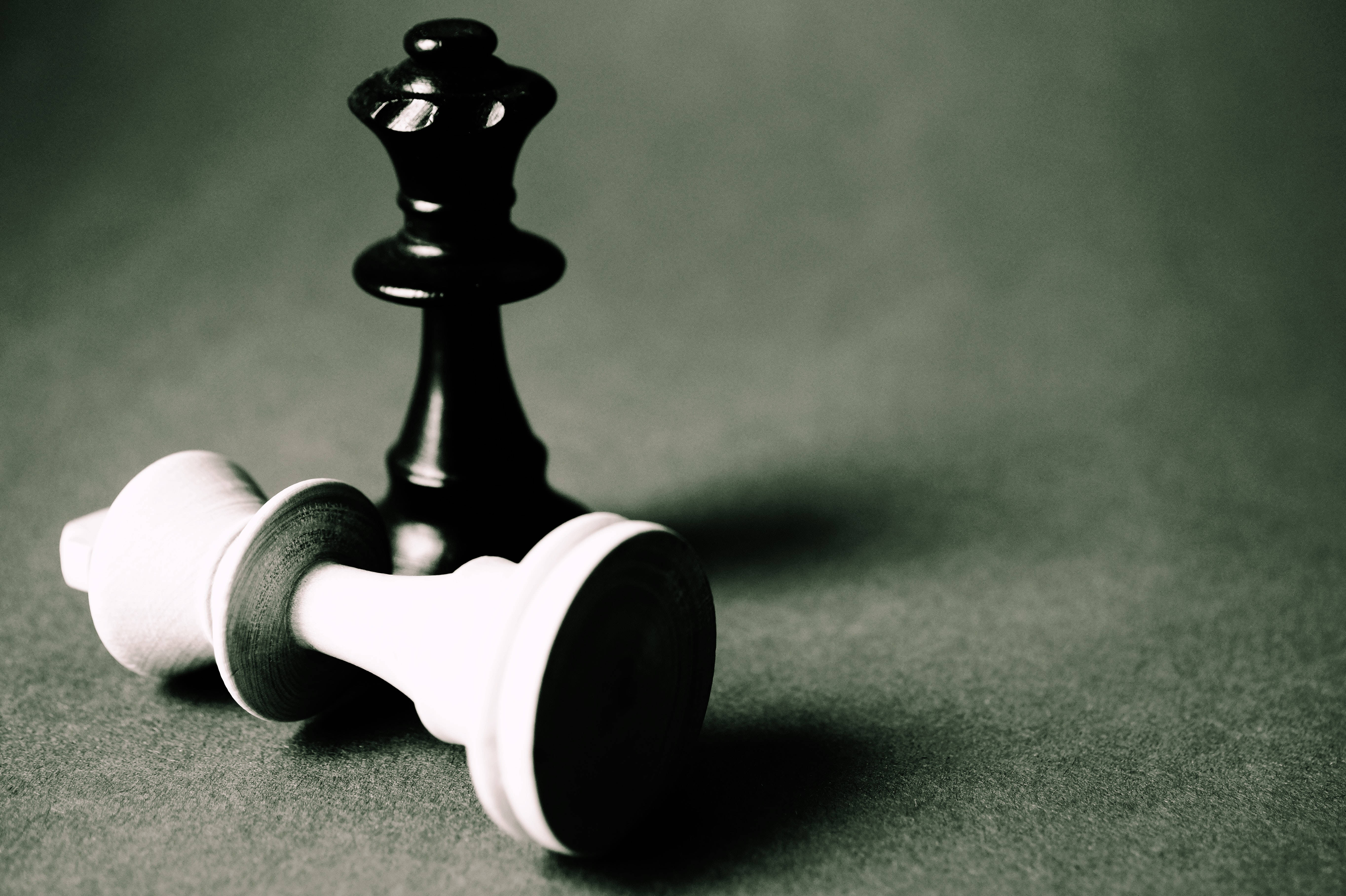 黑白 桌布 壁紙 — 一個黑色西洋棋國王勝利地站在一個倒下的白色皇后之上，背景是柔和的綠色氈面。