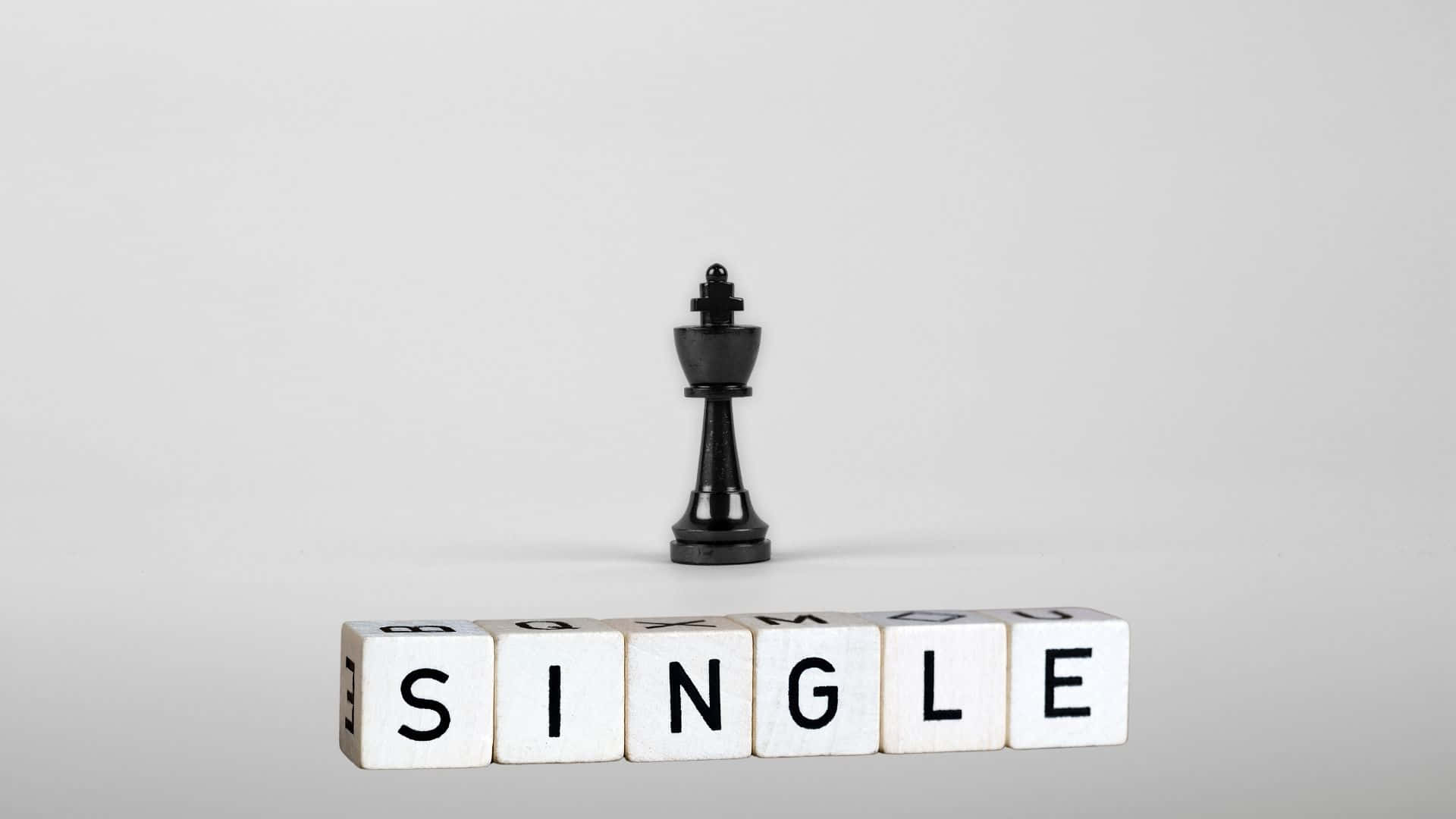 Single 桌布 壁紙 — 一個黑色西洋棋國王獨自站立在由白色木塊拼成的「SINGLE」一詞上方，背景為純灰色。