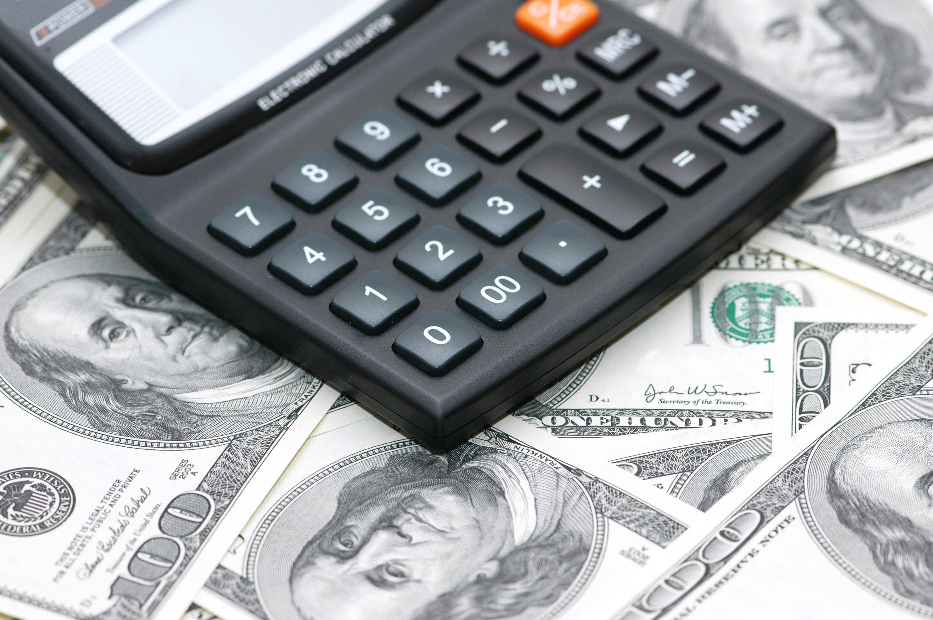 Accounting 桌布 壁紙 — 一個黑色計算機放在散落的一百美元鈔票上，鈔票上有班傑明·富蘭克林的肖像。