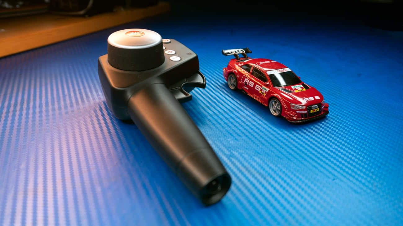 Rc Cars 桌布 壁紙 — 一個黑色賽車控制器和紅色Audi RS5玩具車放在藍色紋理表面上，在聚焦燈光下。