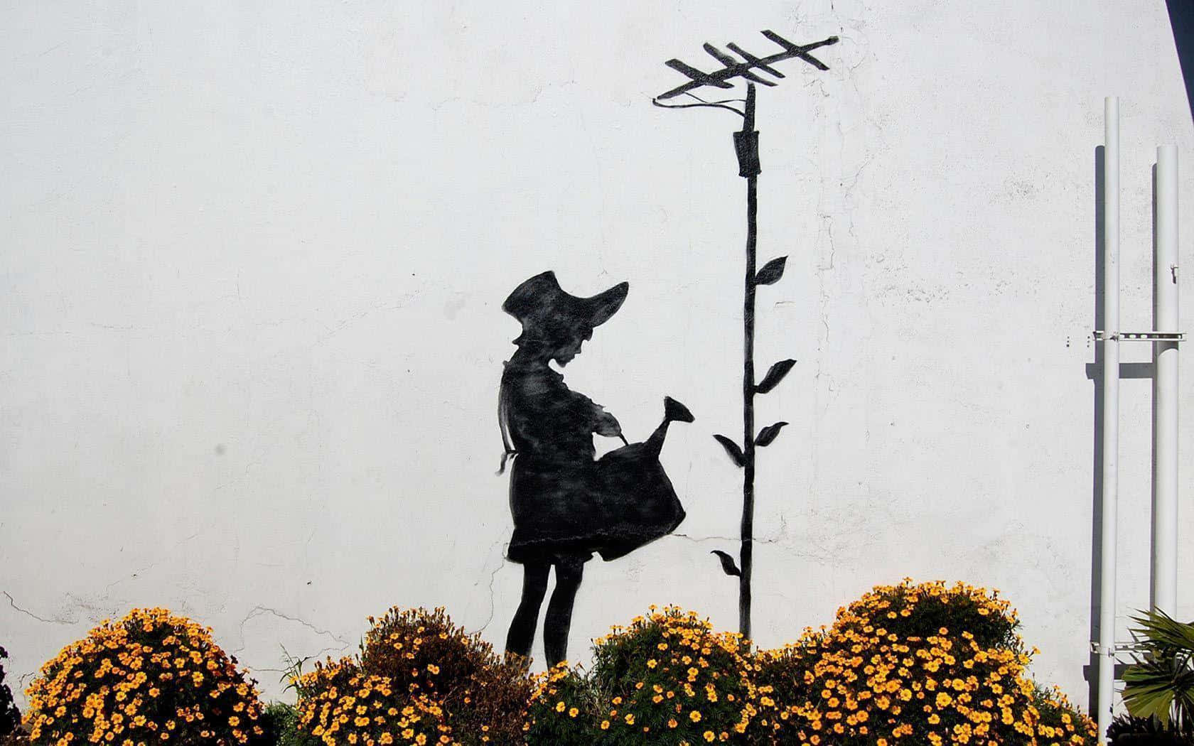 Banksy 桌布 壁紙 — 一個黑色金屬剪影的女孩正在澆灌一株帶有天線頂端的高大植物，站在白色牆壁前，周圍環繞著鮮豔的黃色花朵。