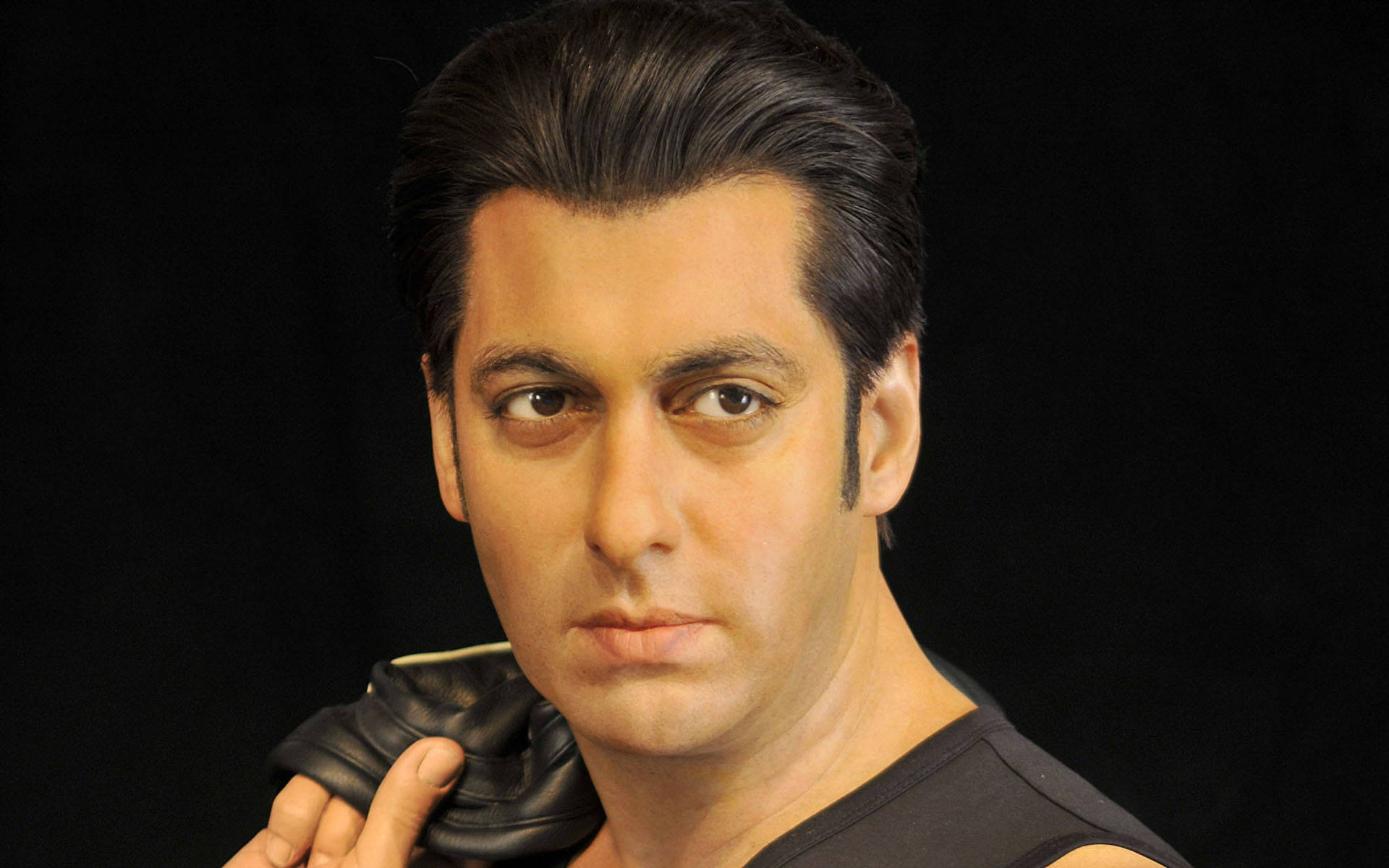 Salman Khan 桌布 壁紙 — 一個黑髮、眼神銳利的男人，在純黑色背景前拿著一隻黑色手套。