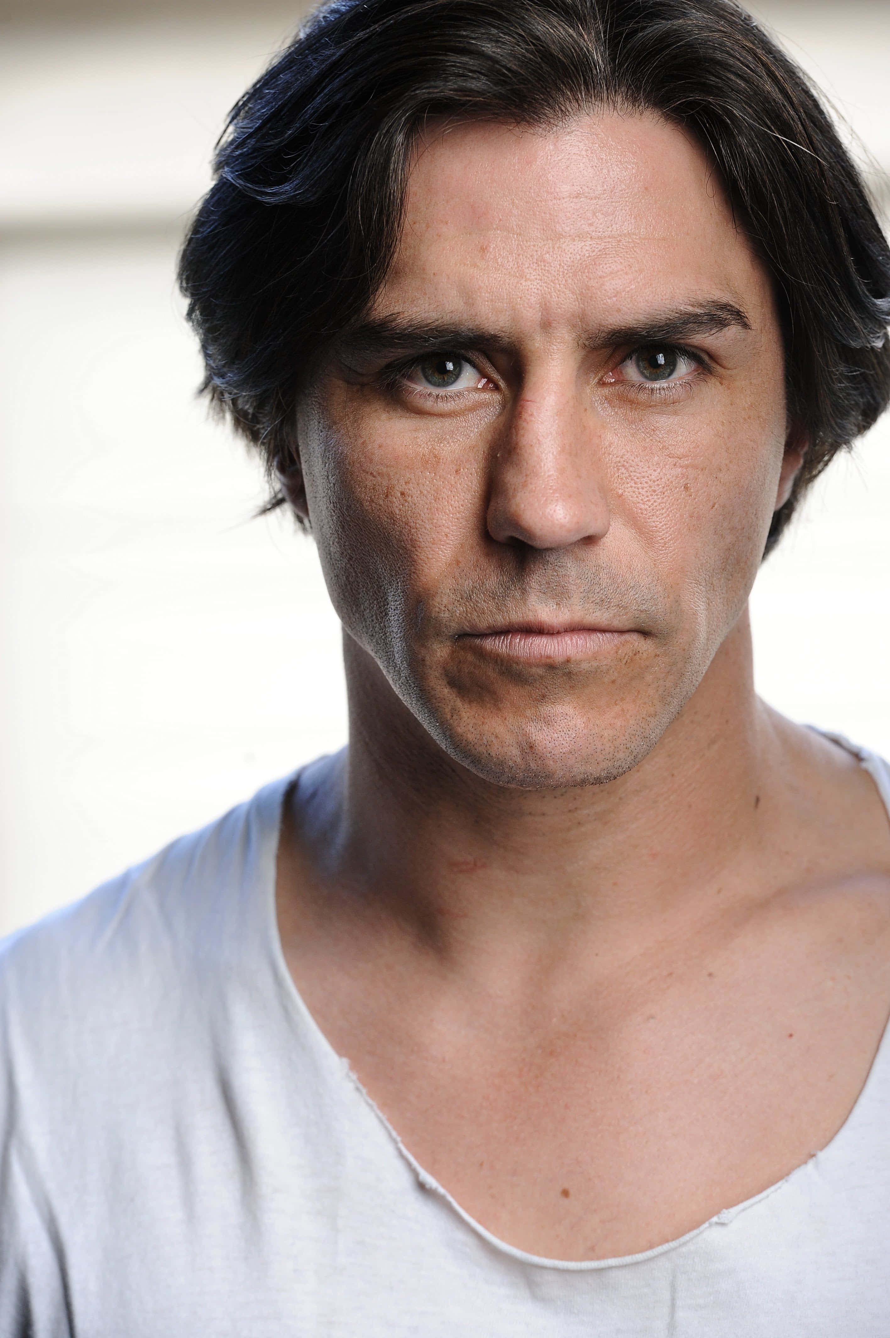 actor 桌布 壁紙 — 一個黑髮、眼神銳利的男子穿著白色T恤，在純色背景前的特寫肖像。