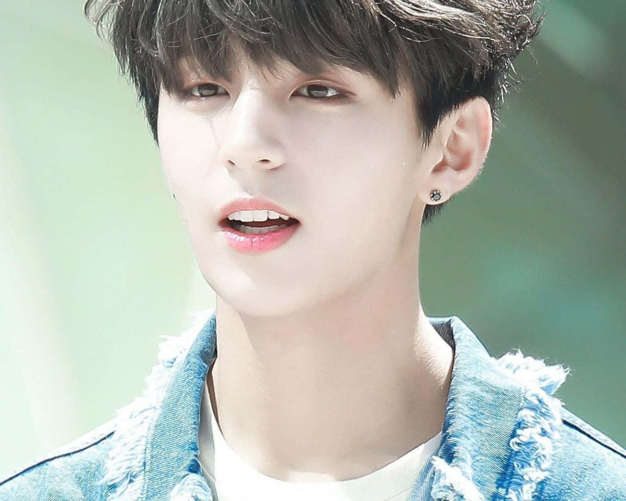 Jungkook 桌布 壁紙 — 一個黑髮、身穿牛仔外套的年輕男子，在模糊的綠色背景下，帶著柔和的表情向上看。