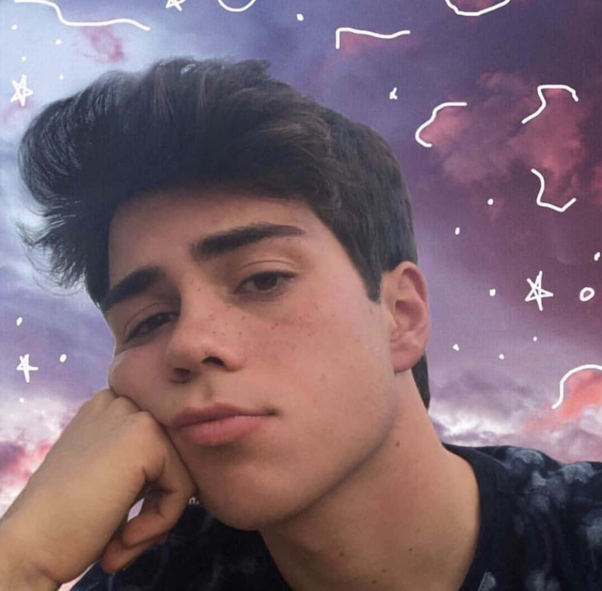 Cute TikTok Profile 桌布 壁紙 — 一個黑髮年輕男子將下巴擱在手上，背景是夢幻的紫色天空，上面有白色塗鴉星星和雲朵。