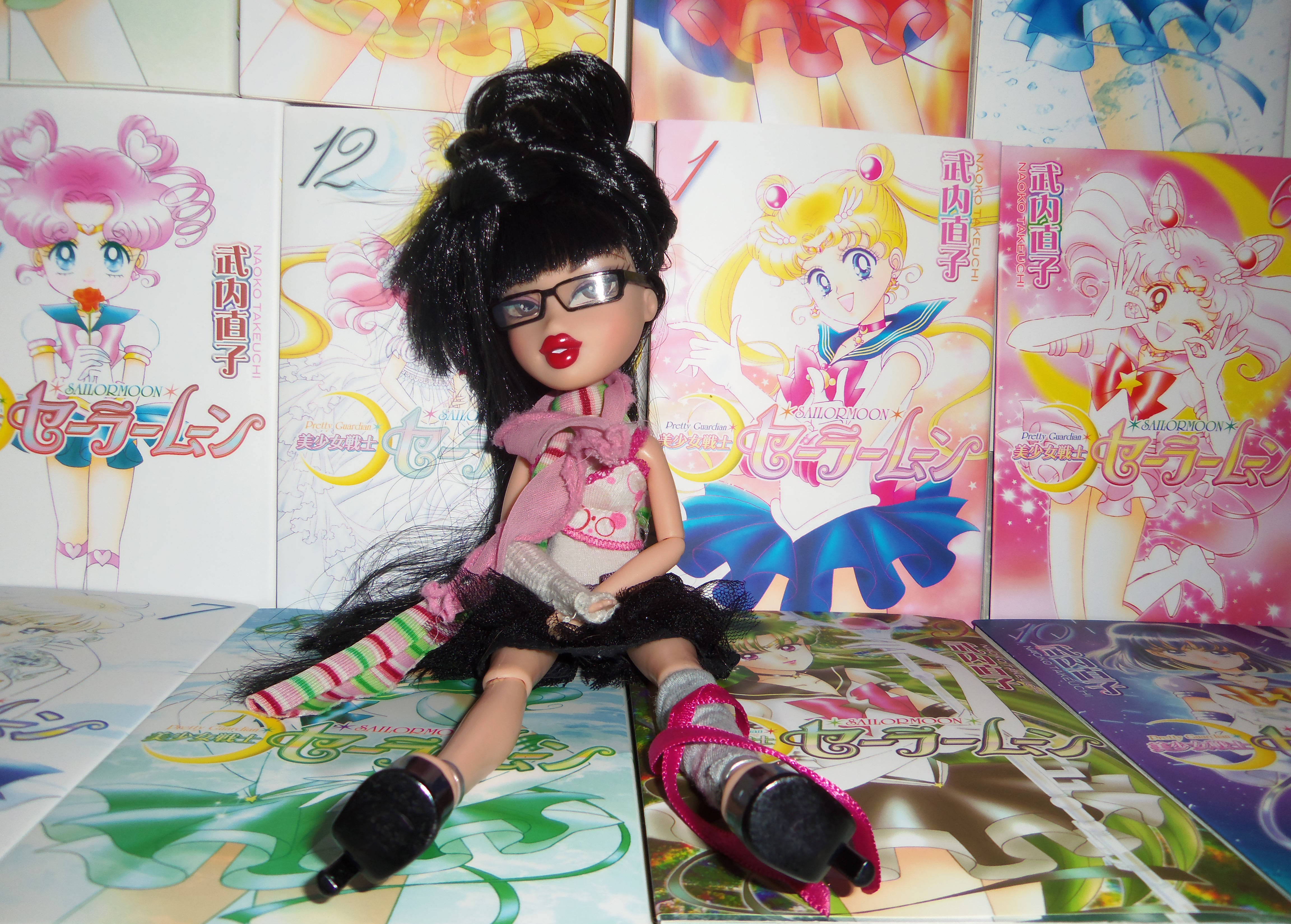 bratz 美學 桌布 壁紙 — 一個黑髮戴眼鏡和粉紅色圍巾的洋娃娃坐在色彩繽紛的美少女戰士漫畫卷和 poster 中。
