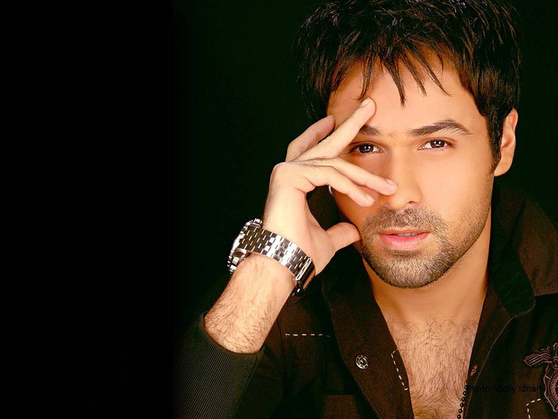 Emraan Hashmi 桌布 壁紙 — 一個黑髮留鬍渣的男人在黑色背景前擺姿勢，手放在臉附近，戴著銀色手錶和深色襯衫。