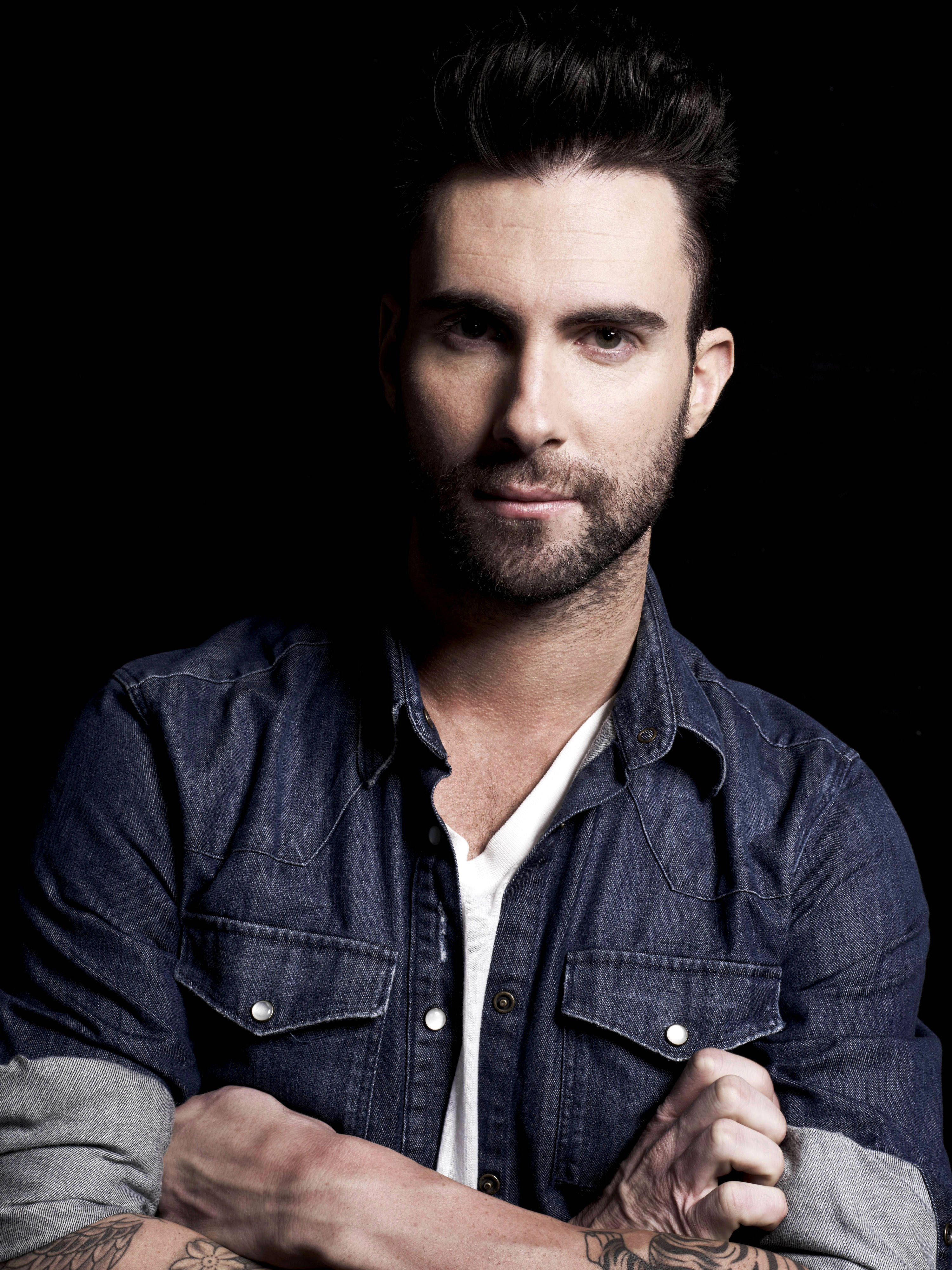 Adam Levine 桌布 壁紙 — 一個黑髮鬍鬚男，在黑色背景前穿著牛仔襯衫內搭白色T恤。