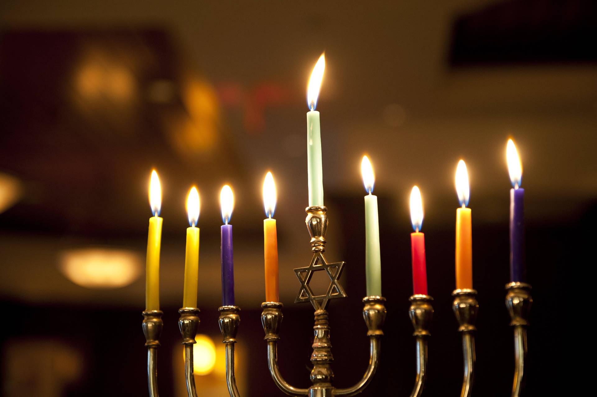 一個 menorah 有九枝點燃的各種顏色的蠟燭，溫暖地發光。 — 光明節 GIF 壁紙