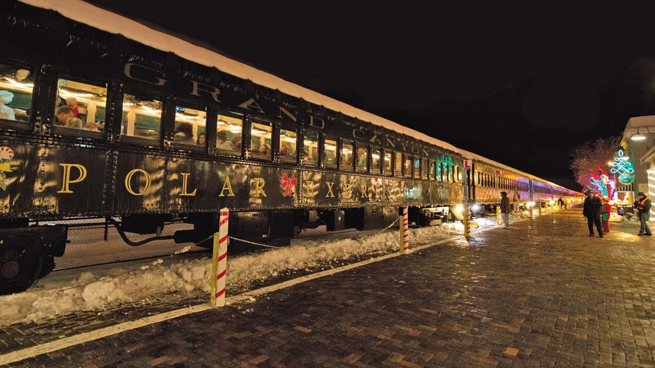 Polar Express 桌布 壁紙 — 一列宏偉的北極特快列車在夜間雪中溫暖地發光，乘客在節日磚砌月台旁望向窗外。