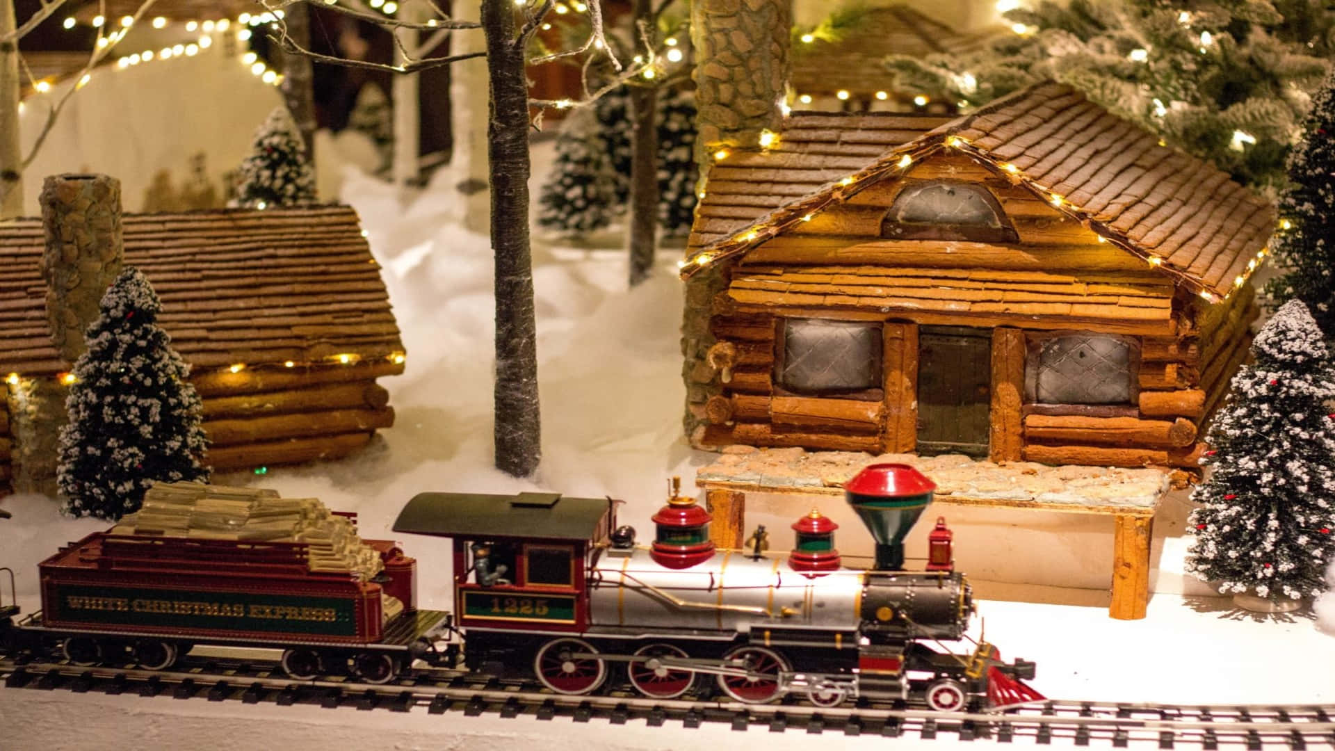 節日 桌布 壁紙 — 一列寫有 White Christmas Express 的節日微型火車，駛過積雪的木屋和裝飾著閃爍仙女燈的松樹。
