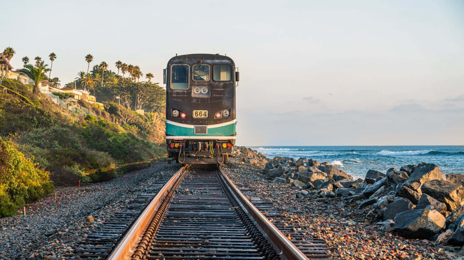 攝影 桌布 壁紙 — 一列復古火車沿著岩石海岸和棕櫚樹懸崖環繞的海岸軌道在黃金時段接近。