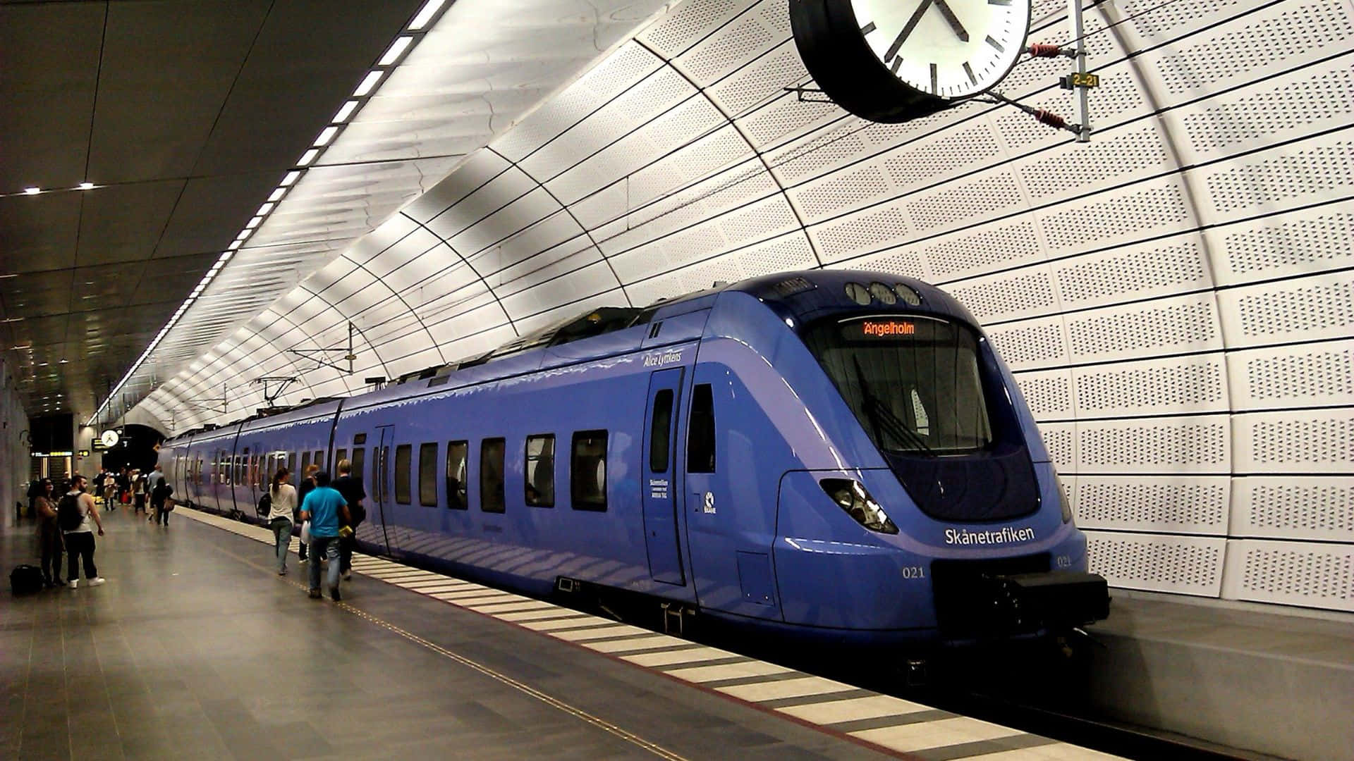 地鐵 桌布 壁紙 — 一列時尚的藍色列車抵達現代化的地下車站，乘客在明亮的螢光燈下於月台等候。