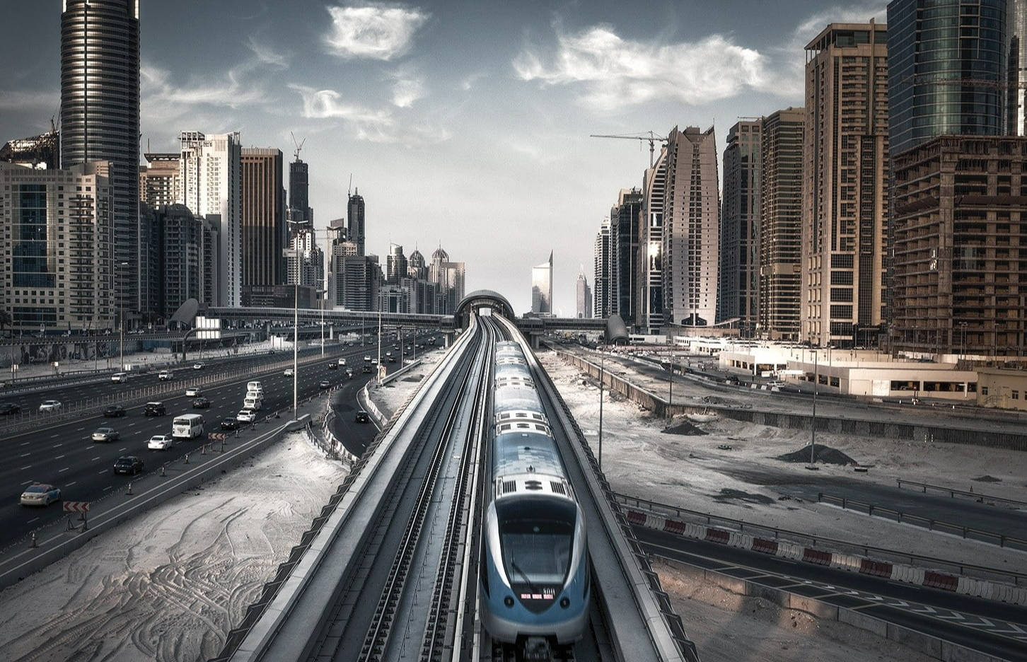 Arab 桌布 壁紙 — 一列時尚的藍色地鐵列車在戲劇性的多雲天空下，穿過兩旁高聳摩天大樓的未來主義城市峽谷飛馳。