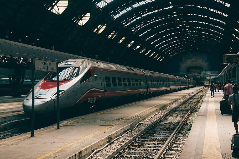 transportation 桌布 壁紙 — 一列時尚的銀紅色高速列車停靠在宏偉的拱形車站月台上，旅客和復古標誌在溫暖的金色燈光下。