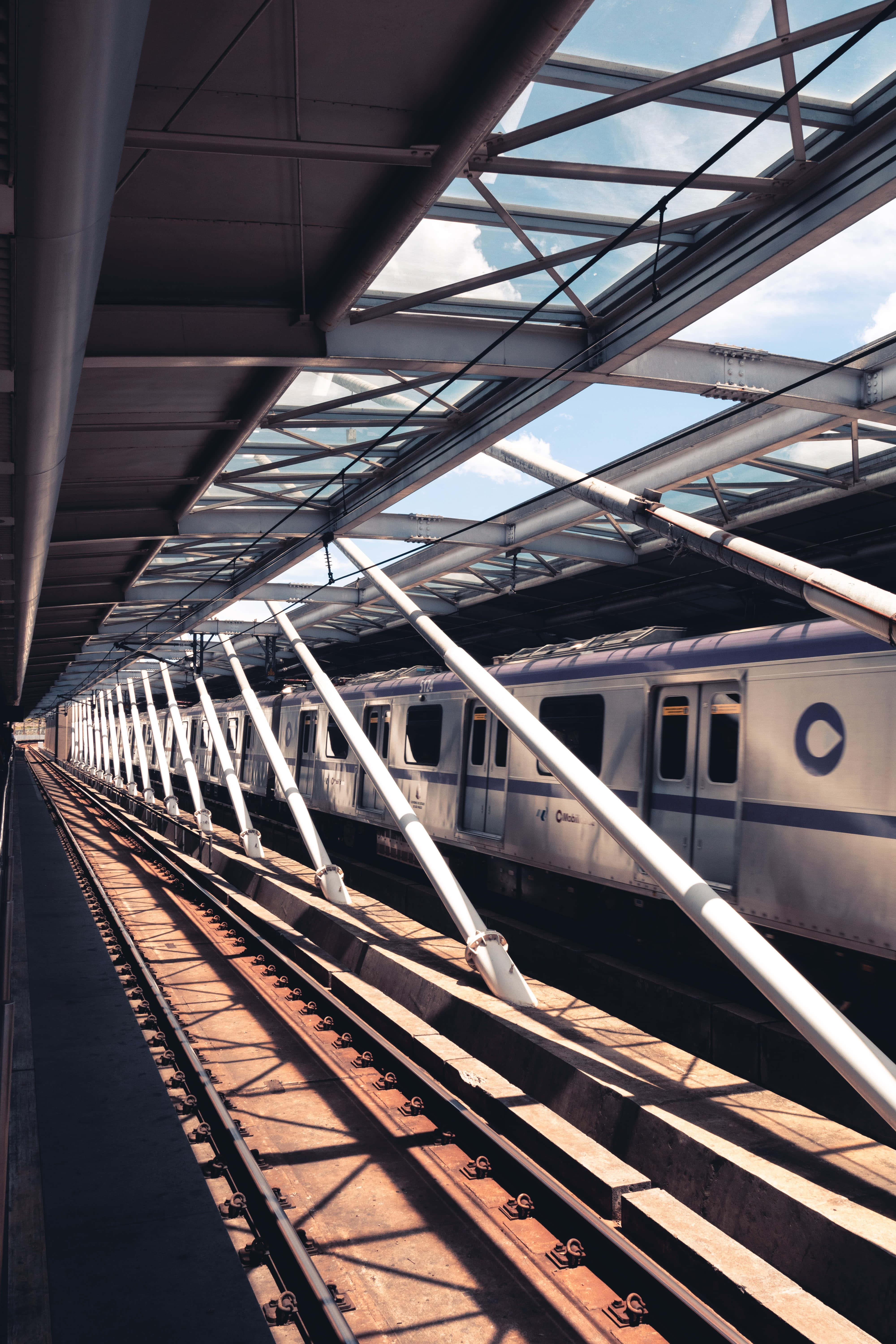 Metro 桌布 壁紙 — 一列時尚的銀色列車停在高架車站的玻璃和鋼製簷篷下，沐浴在明亮的日光中。