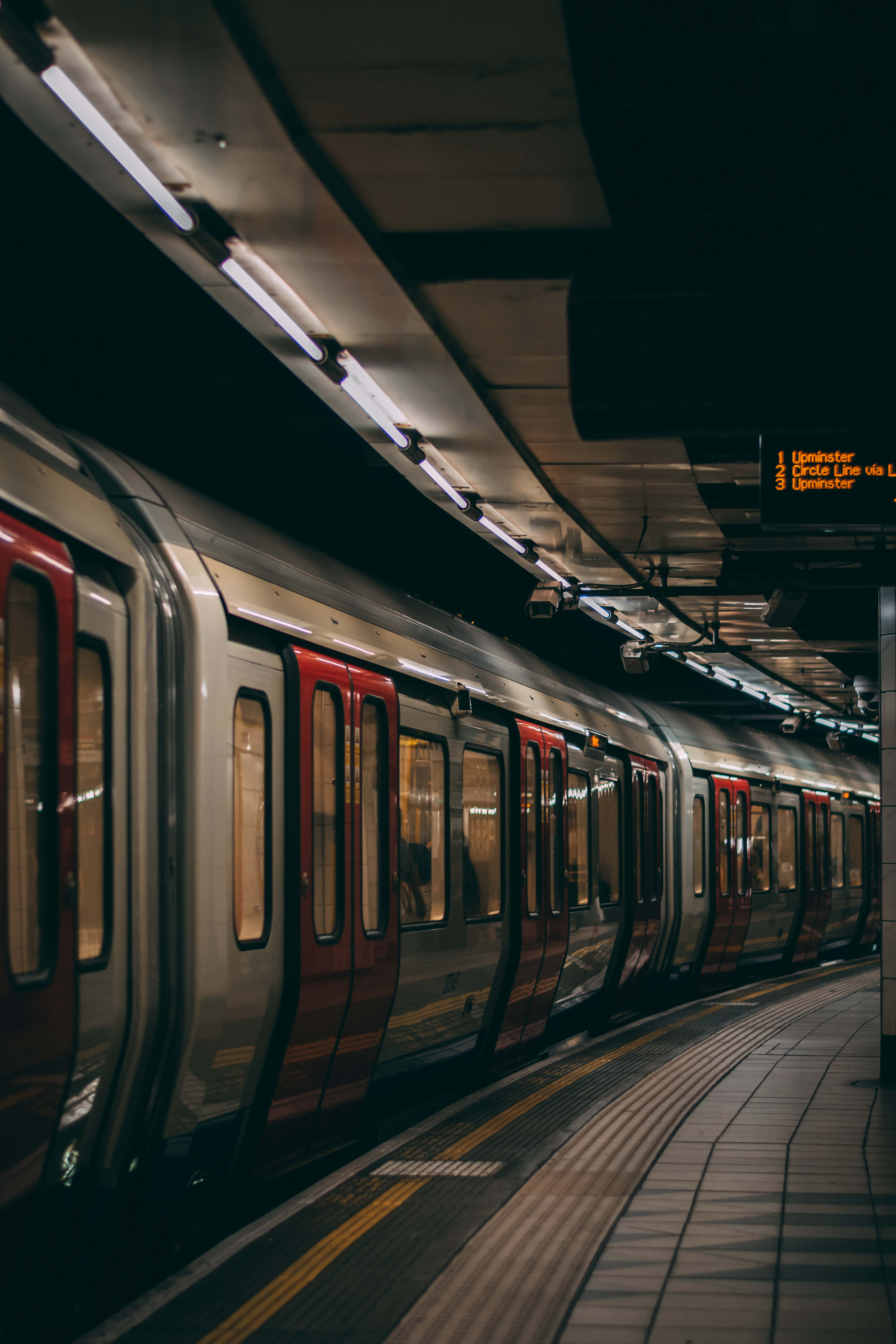 Metro 桌布 壁紙 — 一列時尚的銀色和紅色地鐵列車在昏暗的地下車站月台上，在螢光燈下閃耀。