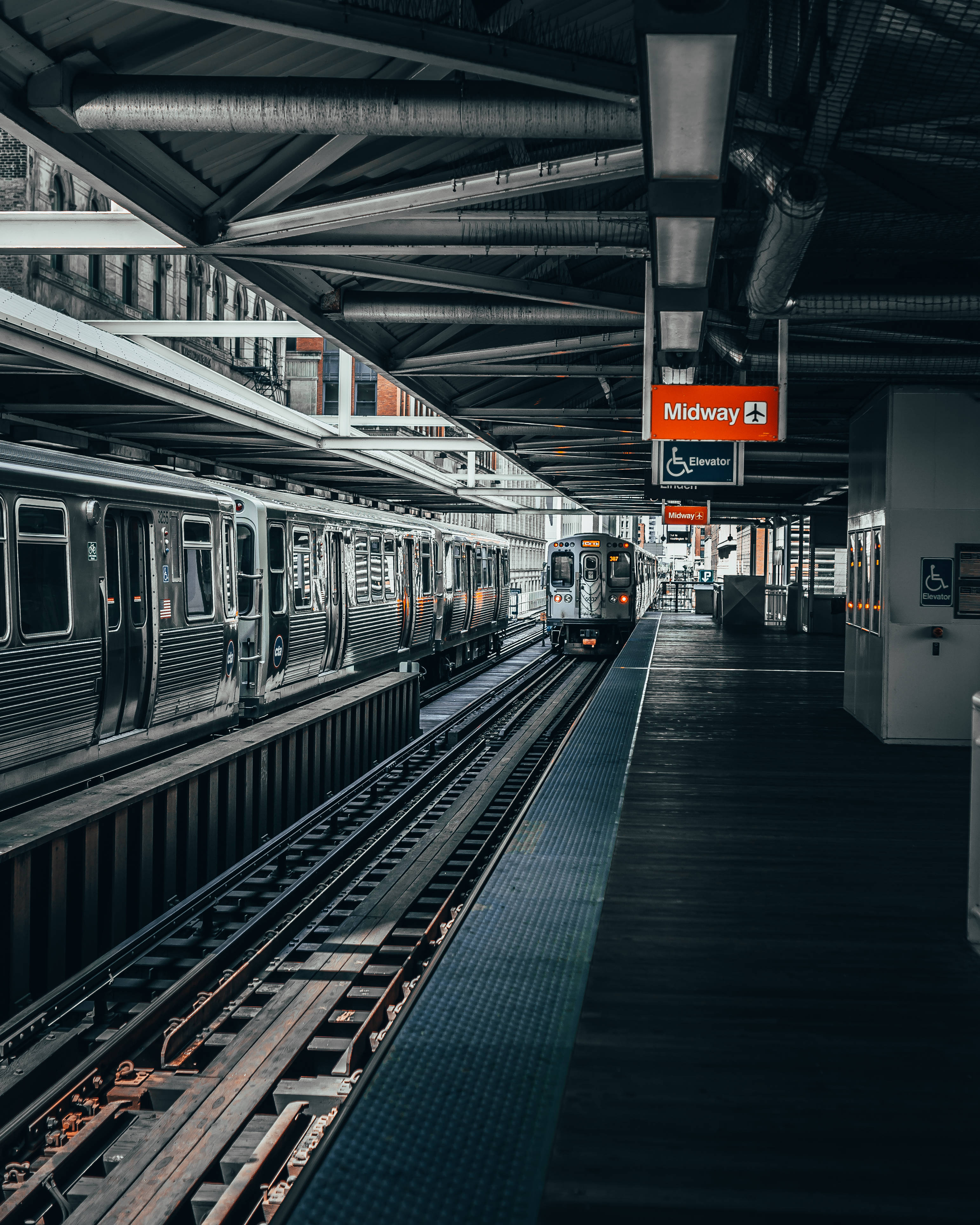 Trendy 桌布 壁紙 — 一列時尚的銀色火車抵達一個燈光昏暗的高架地鐵站，車站有裸露的鋼樑和頭頂上的「Midway」標誌。