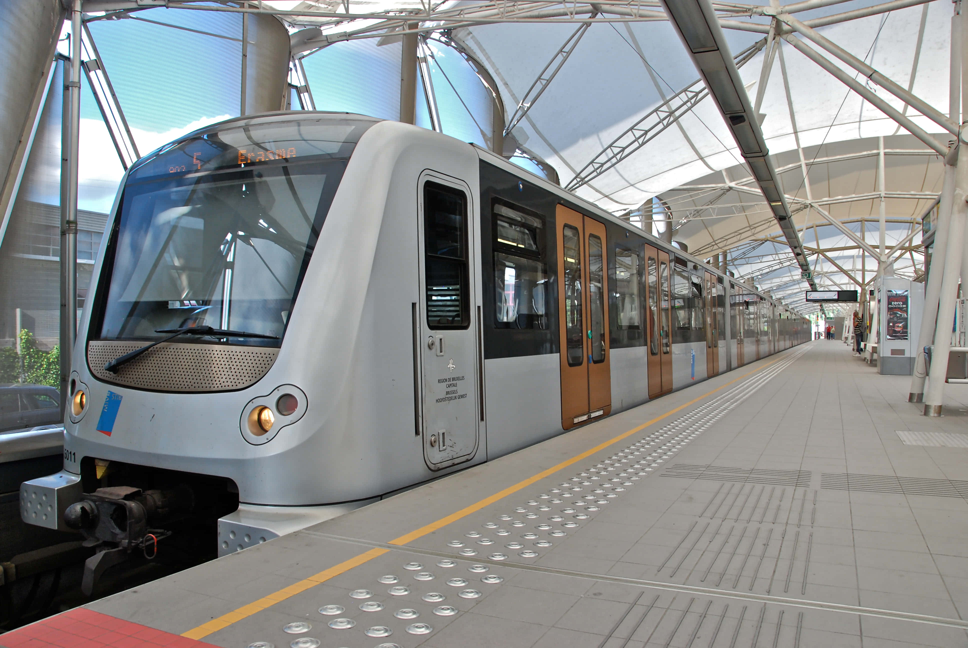 Metro 桌布 壁紙 — 一列時尚的銀色火車配有木門，停靠在玻璃和鋼製天篷下的現代化車站月台上。