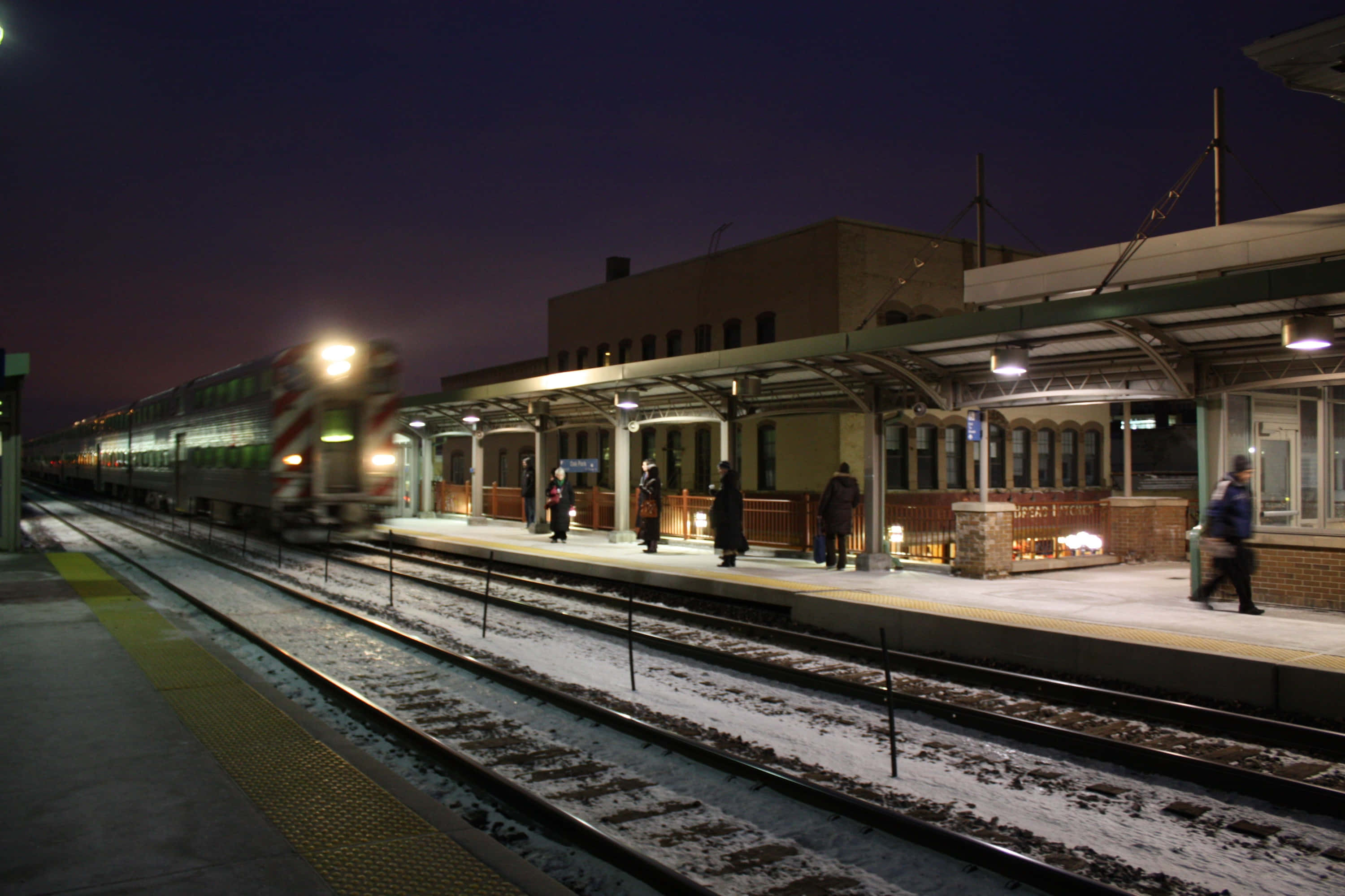 Train Station 桌布 壁紙 — 一列火車在夜燈下抵達積雪的火車站月台，乘客正在等候。