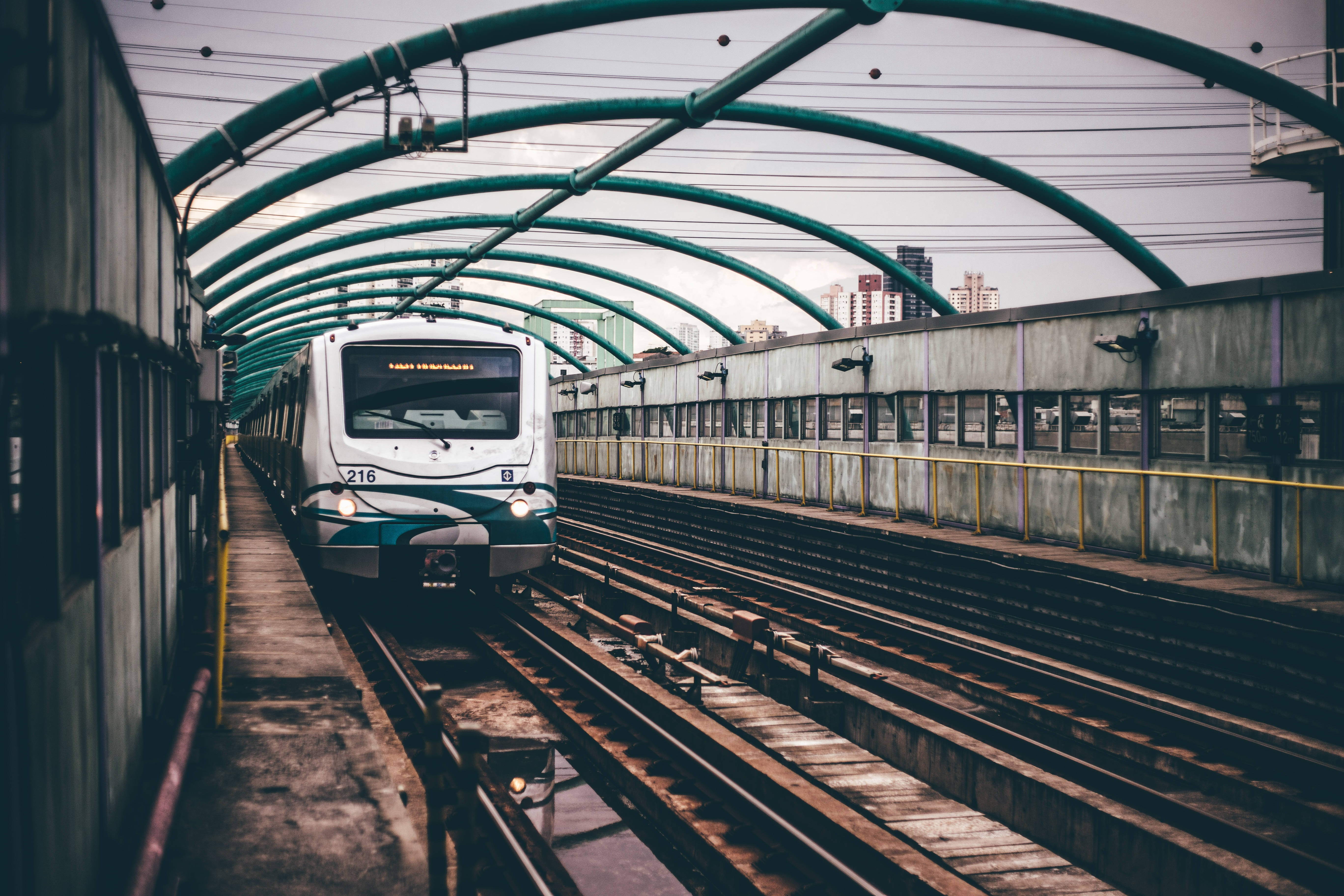 火車 桌布 壁紙 — 一列現代火車在彎曲的綠色金屬天篷下駛近高架城市鐵路軌道。