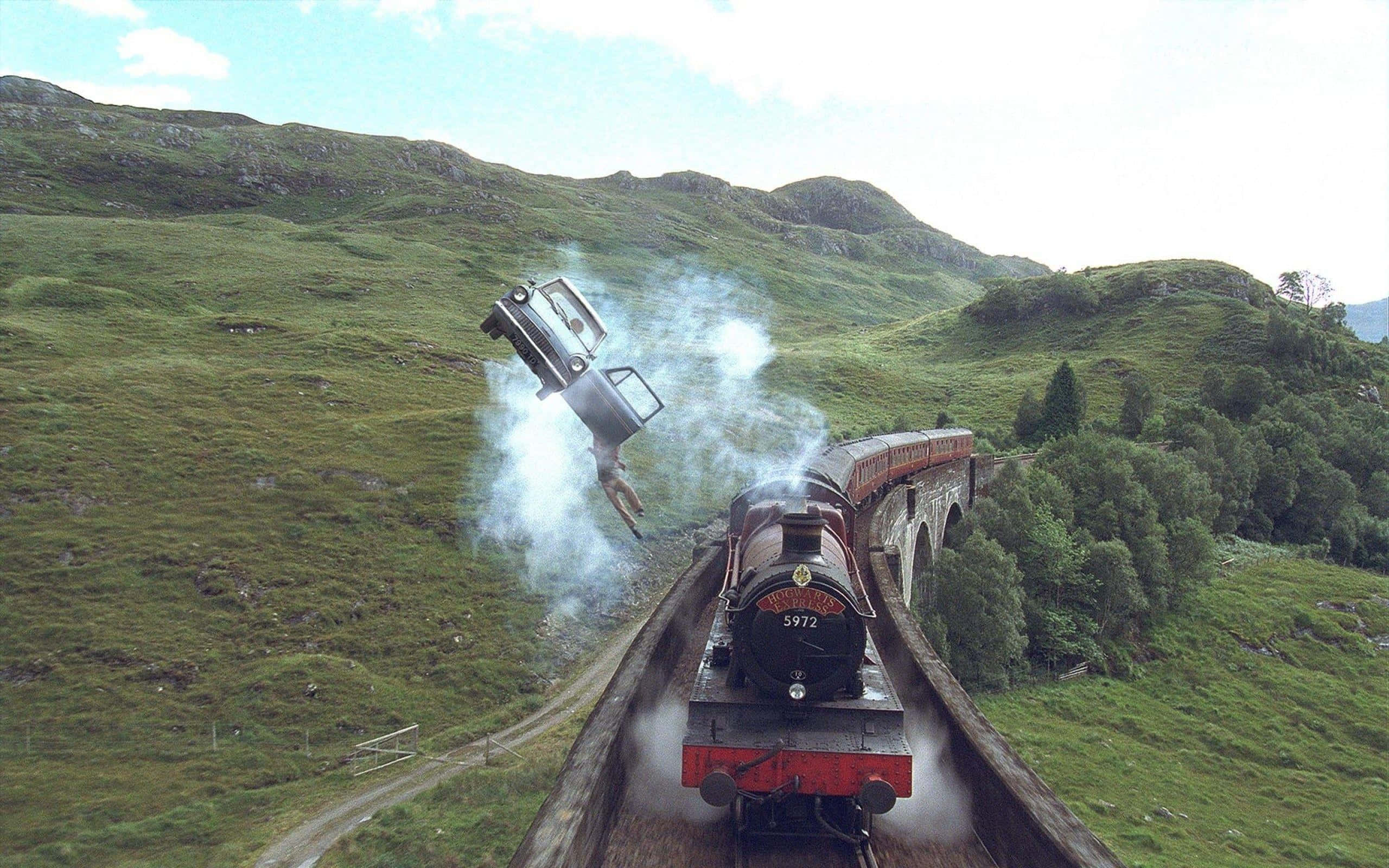 The Hogwarts Express Train 桌布 壁紙 — 一列蒸汽火車在石砌高架橋上疾馳，一輛汽車被無形力量猛烈拋向空中，四周是翠綠的山丘。