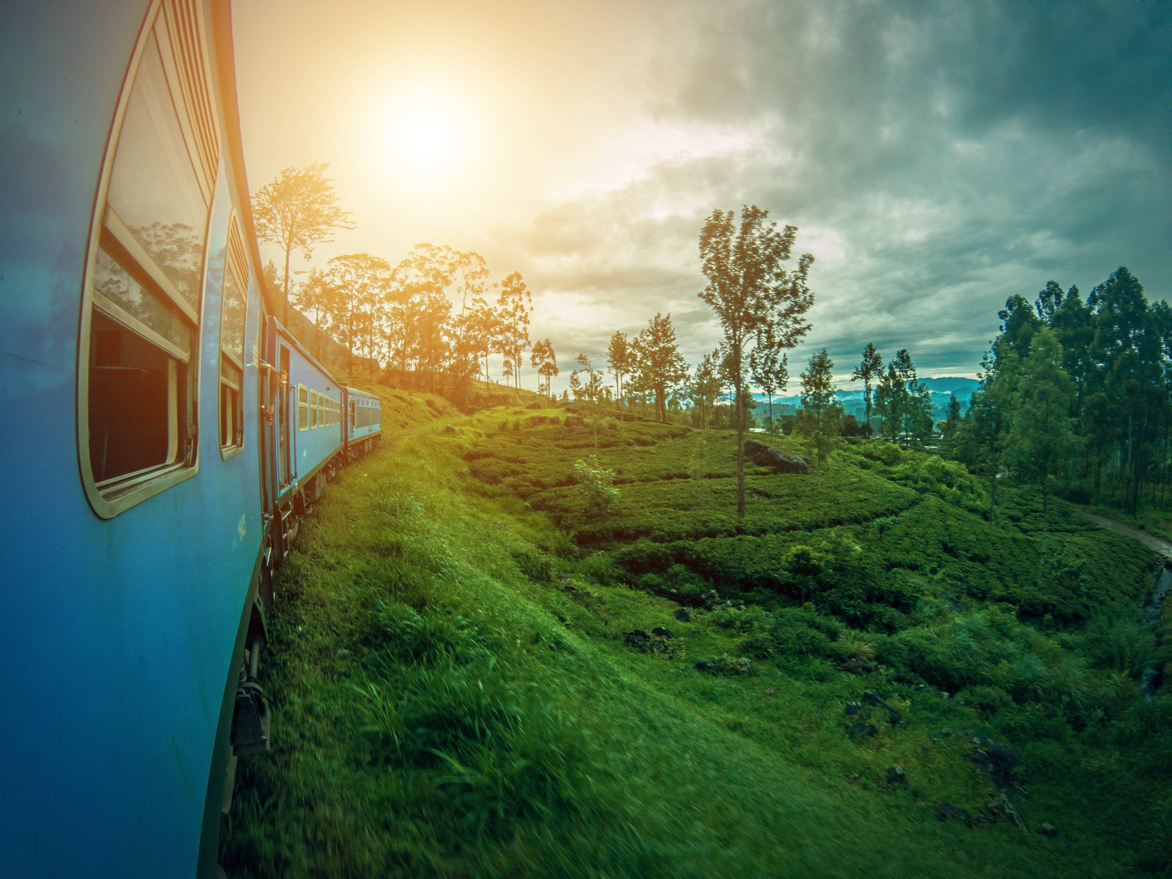 Sri Lanka 桌布 壁紙 — 一列藍色火車在戲劇性的金色日落天空下，滑過鬱鬱蔥蔥的綠色茶園梯田。