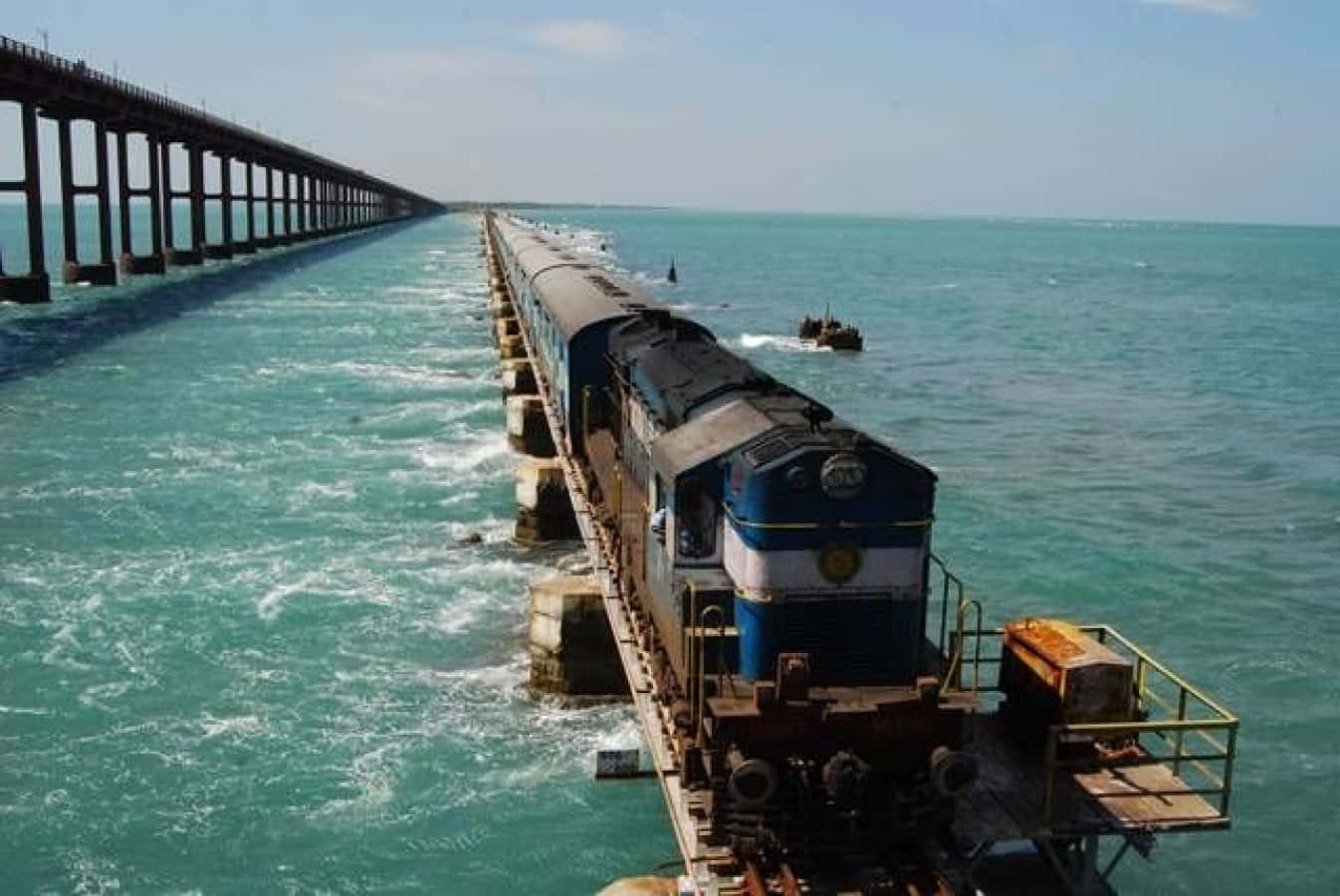 Indian Railway 桌布 壁紙 — 一列藍色火車在晴朗的天空下，沿著長長的碼頭行駛在碧綠色的海面上。
