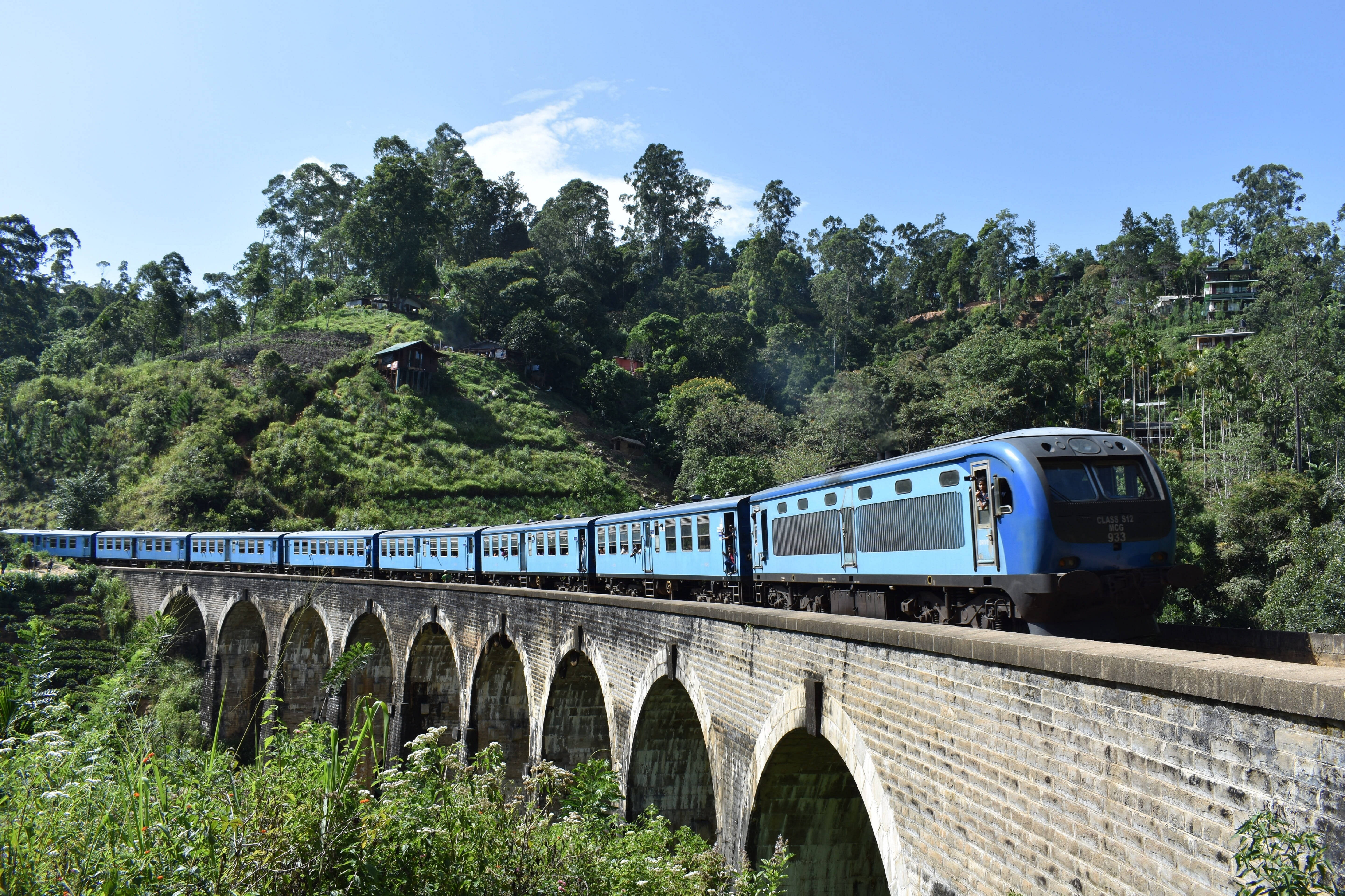 Sri Lanka 桌布 壁紙 — 一列藍色火車穿過石拱橋，越過青翠的山丘，在晴朗的藍天下行駛。