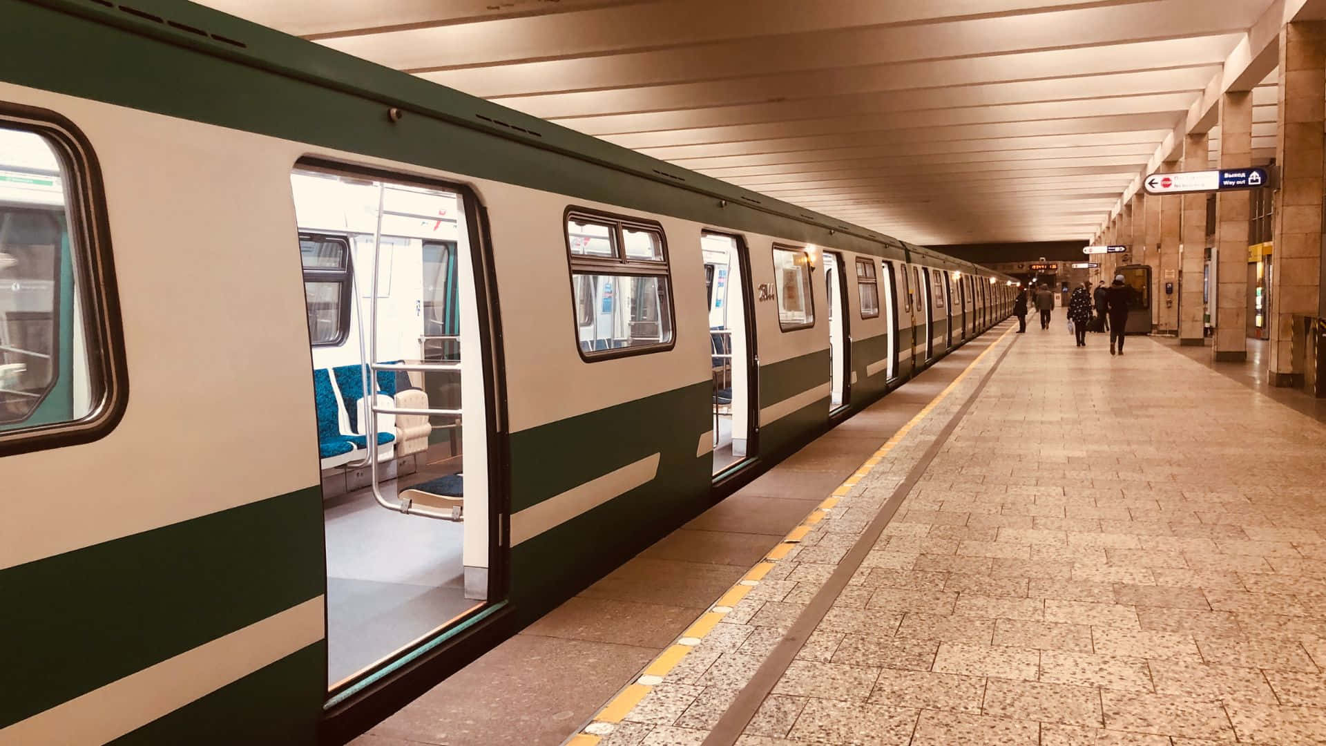 地鐵 桌布 壁紙 — 一列長長的綠色和白色火車停在鋪有瓷磚的地鐵月台上，遠處有乘客在溫暖的人造燈光下行走。