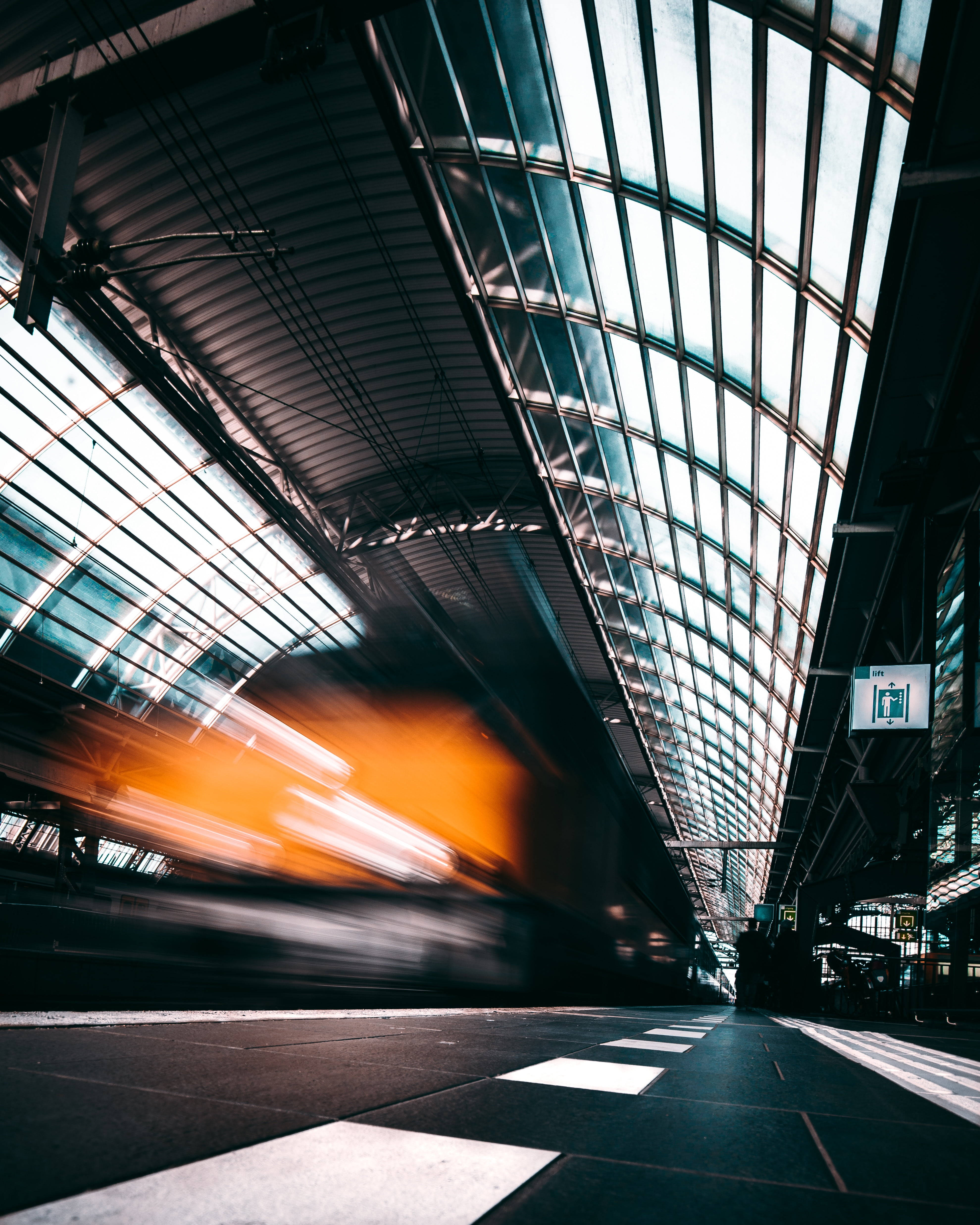 driving fast 桌布 壁紙 — 一列高速行駛的火車在戲劇性的低角度燈光下，拖著橙色光線穿過寬闊的玻璃屋頂車站。