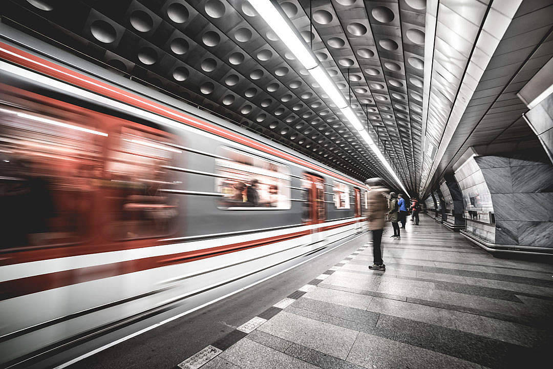 Moving 桌布 壁紙 — 一列高速行駛的紅色地鐵列車在一個時尚現代、鋪有幾何圖案瓷磚地板和圓形天花板燈的車站中，模糊地掠過一位孤獨等候的乘客。