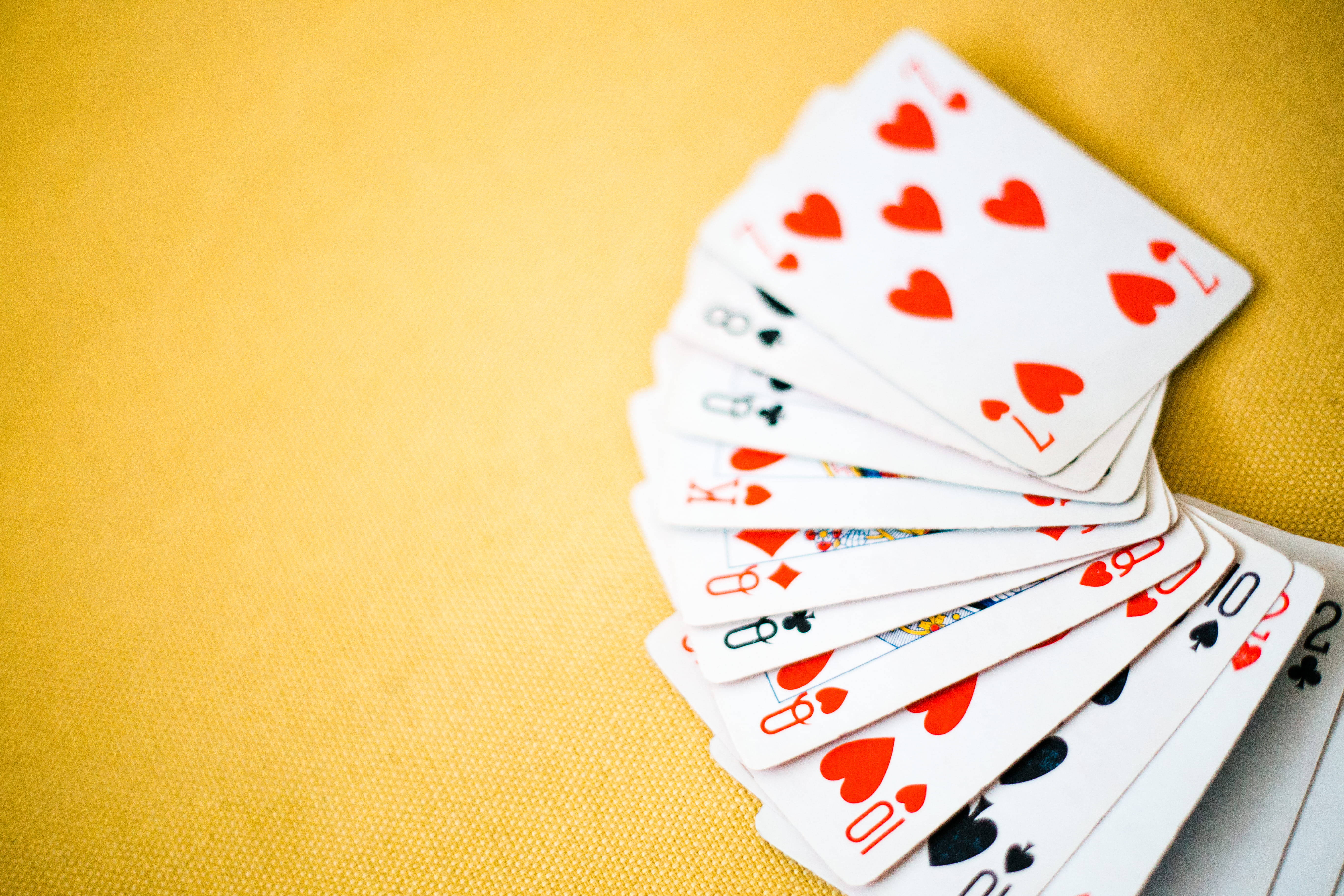Playing Cards 桌布 壁紙 — 一副以扇形展開的撲克牌，有紅色愛心和黑色花色，放在有紋理的金黃色表面上。