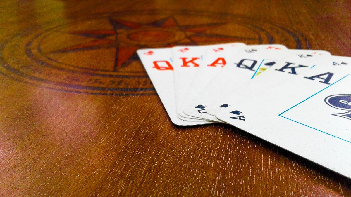 Casino 桌布 壁紙 — 一副扇狀展開的撲克牌，在帶有指南針玫瑰鑲嵌的木桌上顯示紅心同花順。