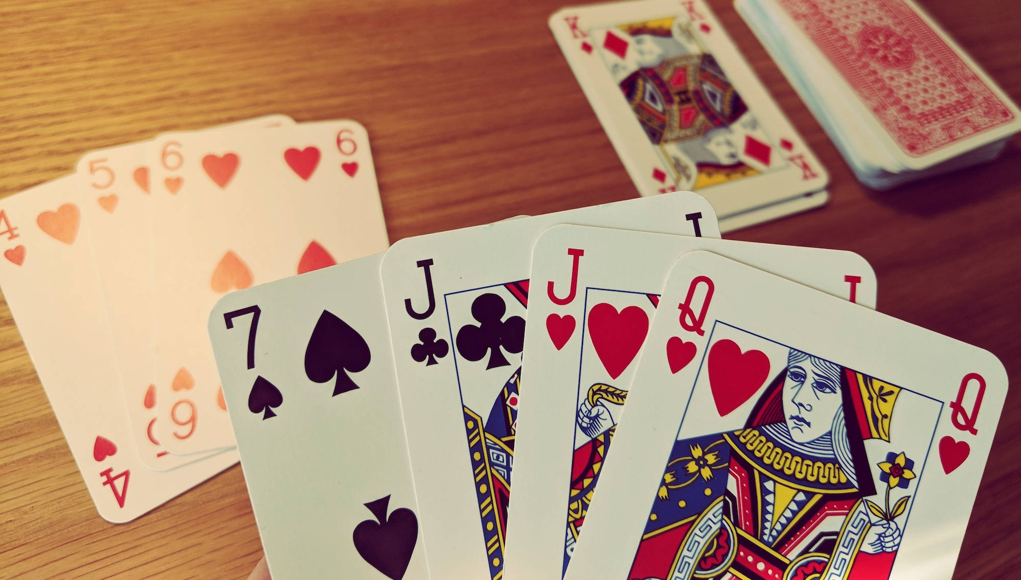 Cards 桌布 壁紙 — 一副撲克牌以扇形展開，包括人頭牌及編號的紅心、黑桃、梅花，放在溫暖的木桌上。