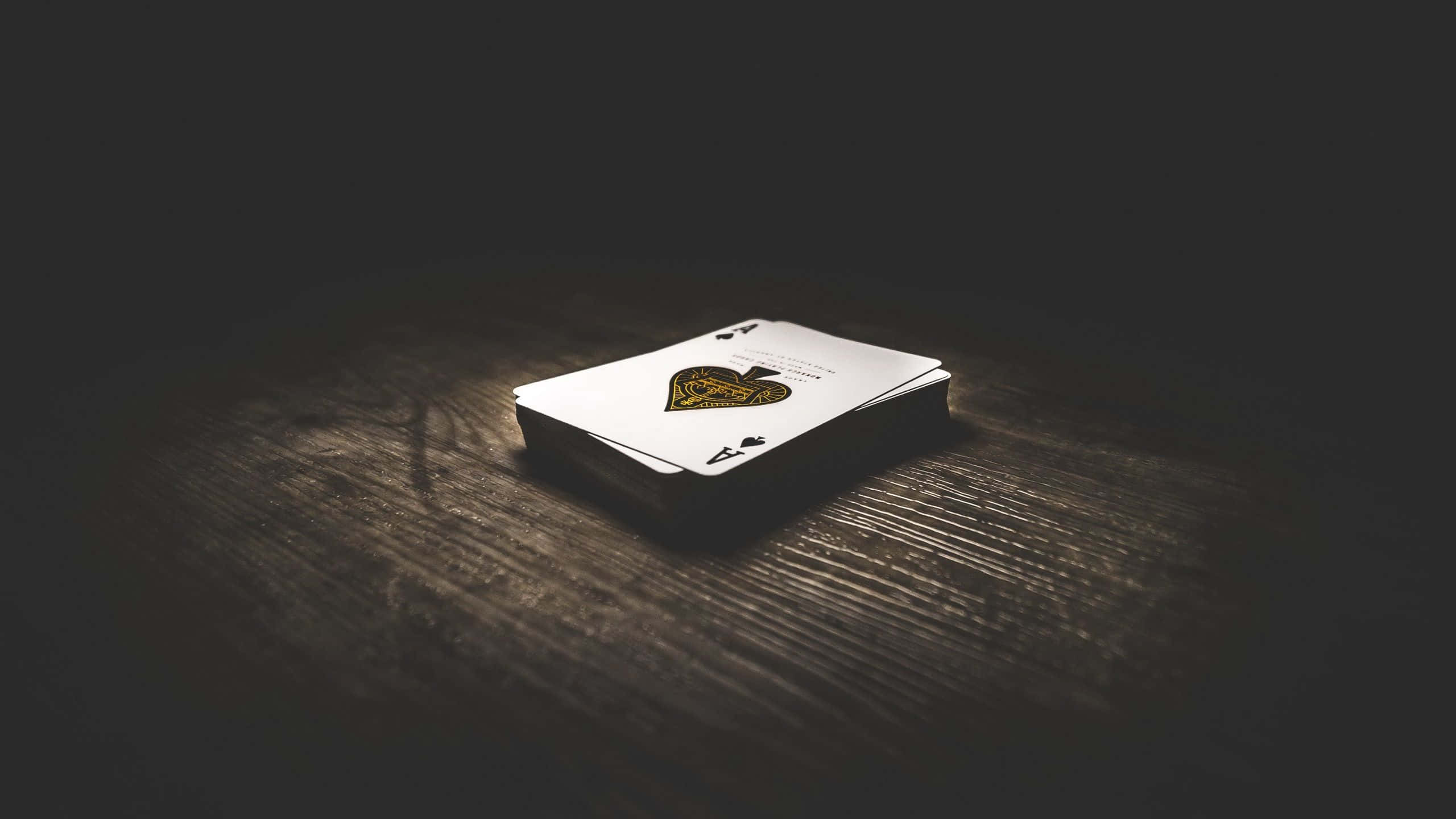 Card Games 桌布 壁紙 — 一副撲克牌放在深色木桌上，處於戲劇性的聚光燈照明下。
