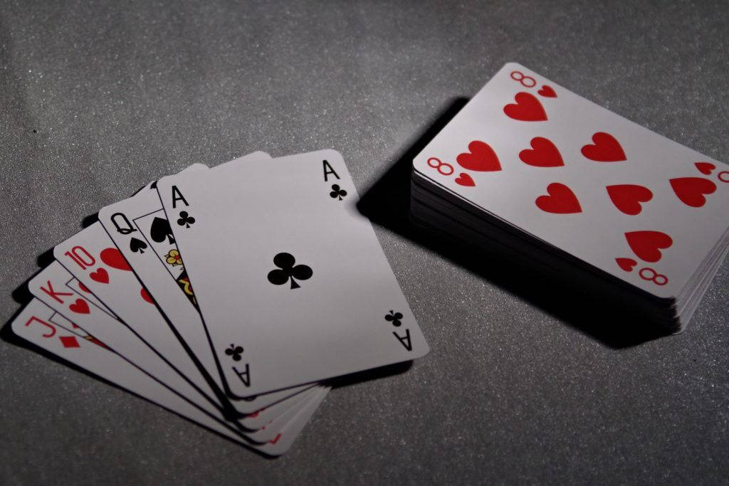 Poker 桌布 壁紙 — 一副攤開成扇形的撲克牌，包括A牌和人頭牌，放在一堆紅色愛心撲克牌旁邊，置於有紋理的灰色表面上。