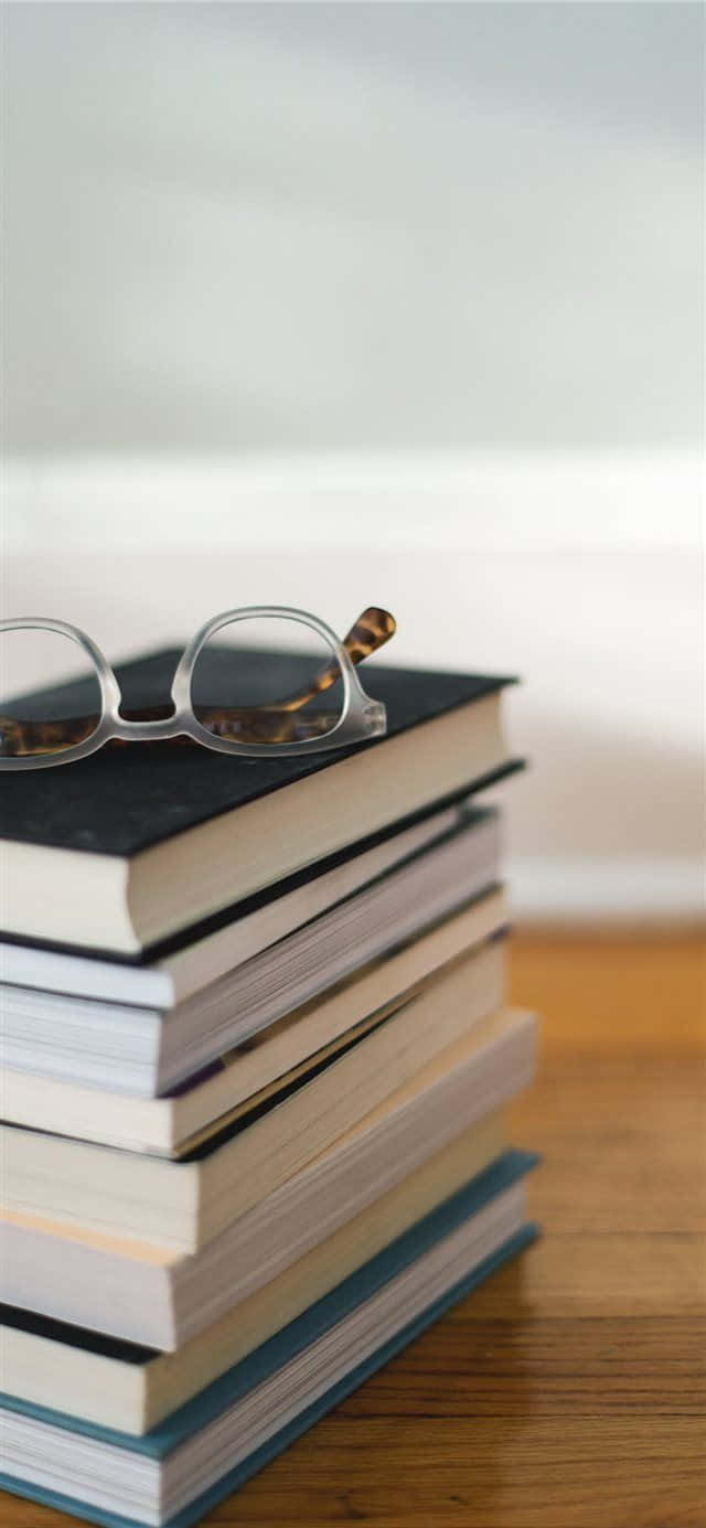 Eyeglass 桌布 壁紙 — 一副玳瑁眼鏡擱在一堆書本上，書本放在木質表面上，有柔和自然光。