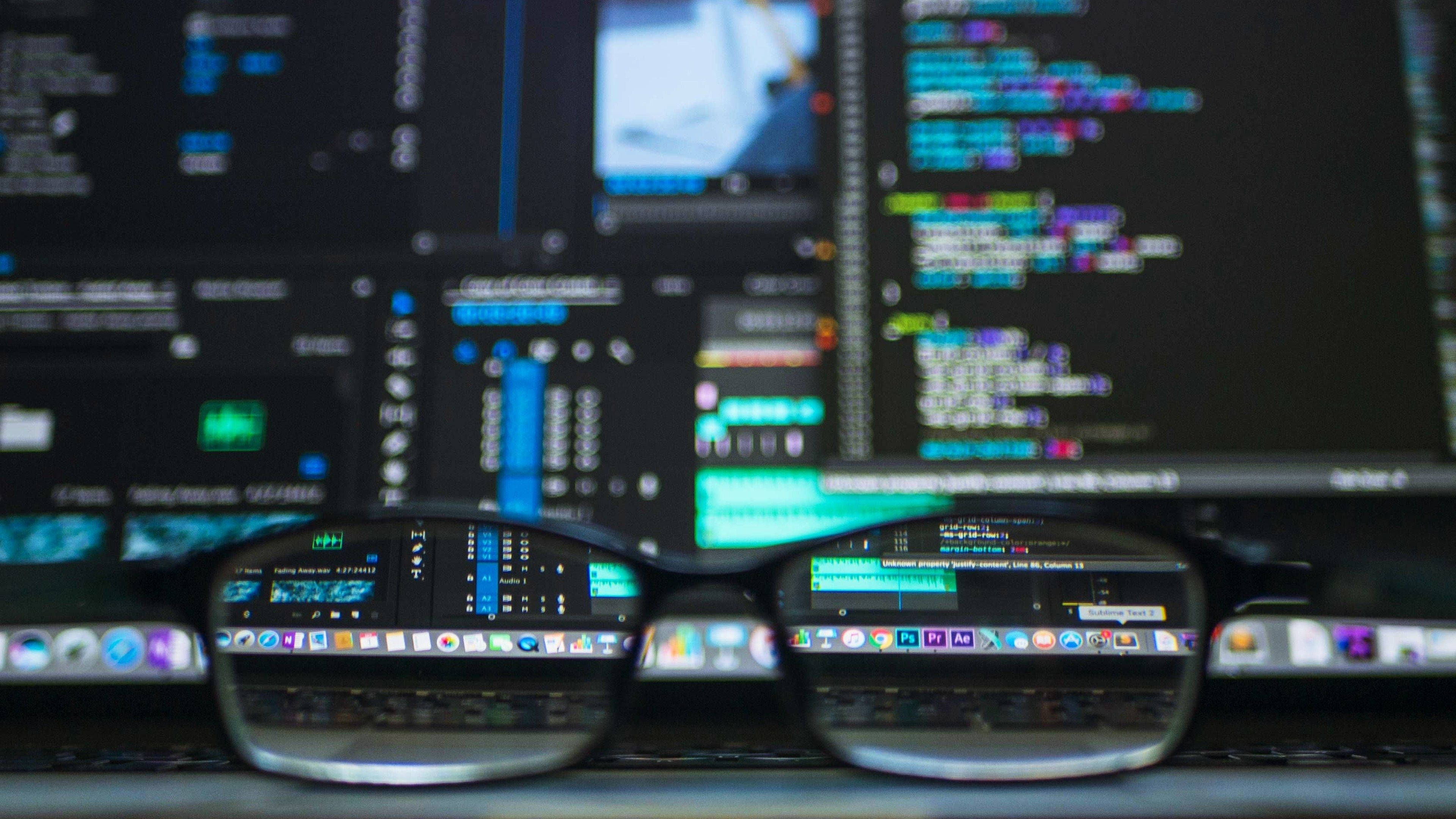 Market 桌布 壁紙 — 一副眼鏡放在桌上，反射出多個電腦顯示器上的彩色程式碼和應用程式圖示。