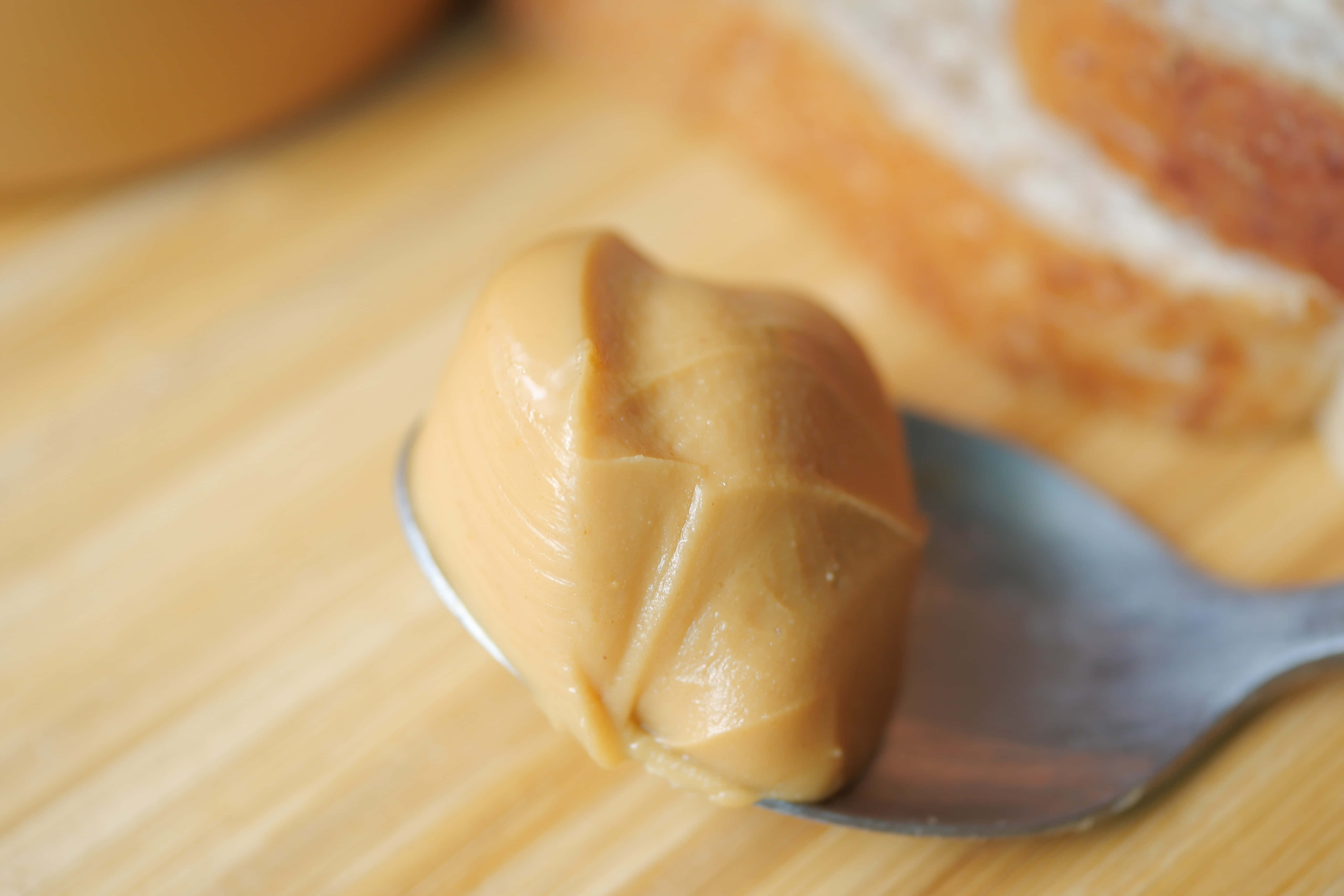 Caramel 桌布 壁紙 — 一匙奶油花生醬放在木質表面上的麵包片旁邊的湯匙上。