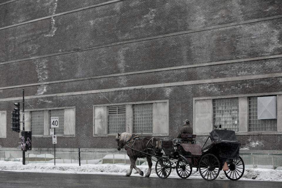Windows 冬季 桌布 壁紙 — 一匹馬拉著馬車沿著積雪的街道行駛，經過一座風化的磚砌建築，天空多雲。