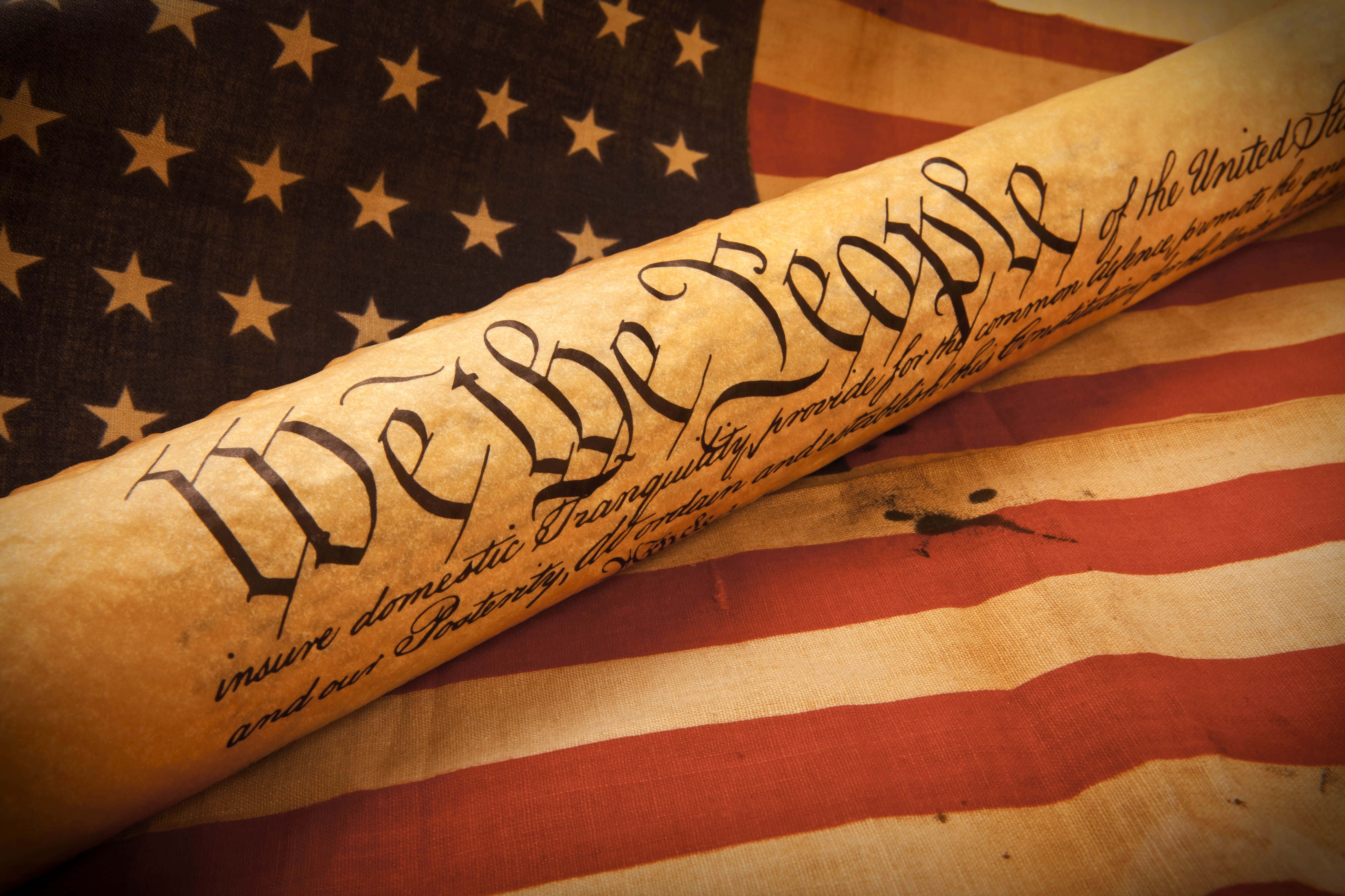 桌布 壁紙 — 一卷刻有「We the People」的美國憲法羊皮紙，放在一面風化的美國國旗上。