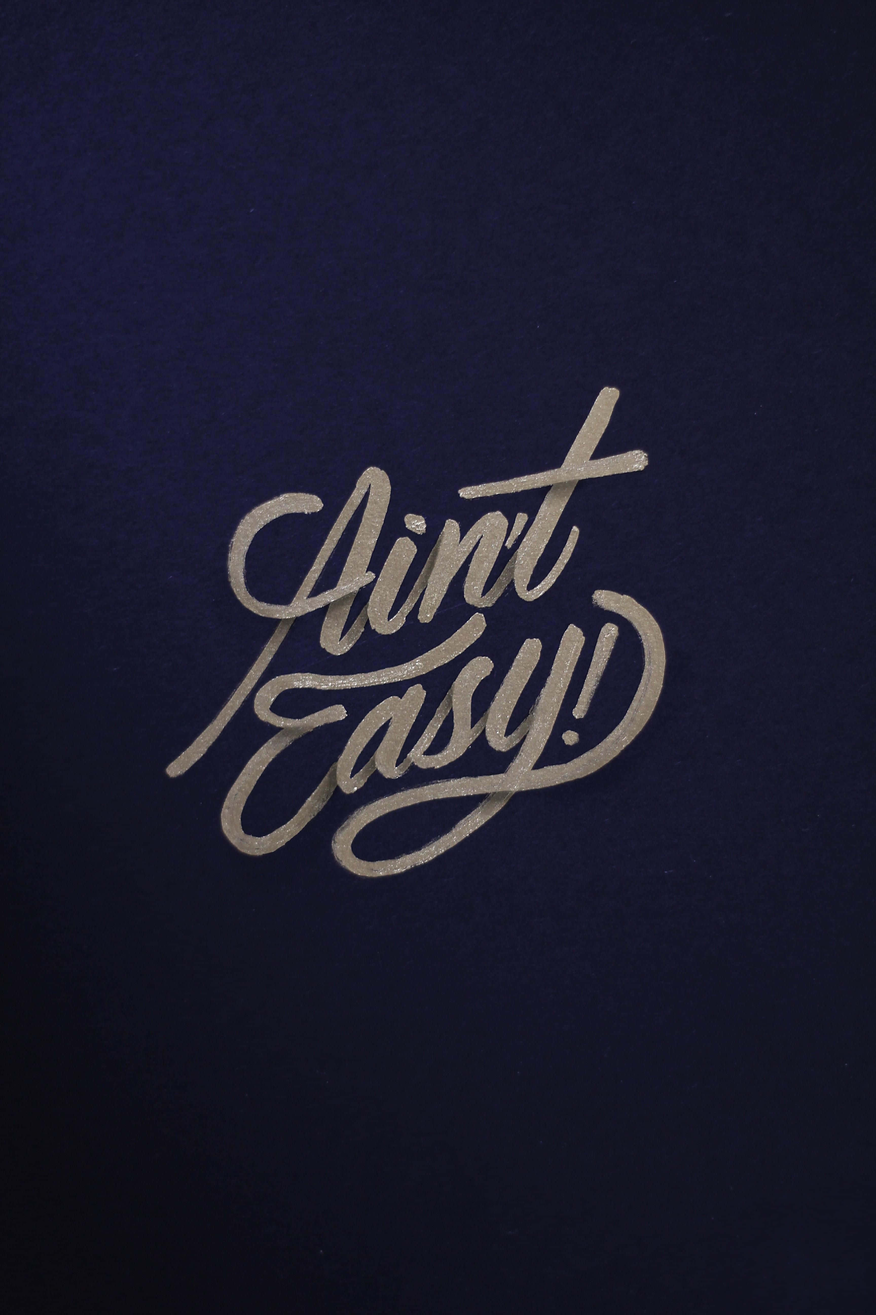 美學 桌布 壁紙 — 一句大膽的銀色草書短語「Ain't Easy!」在深海軍藍紋理背景上發光。