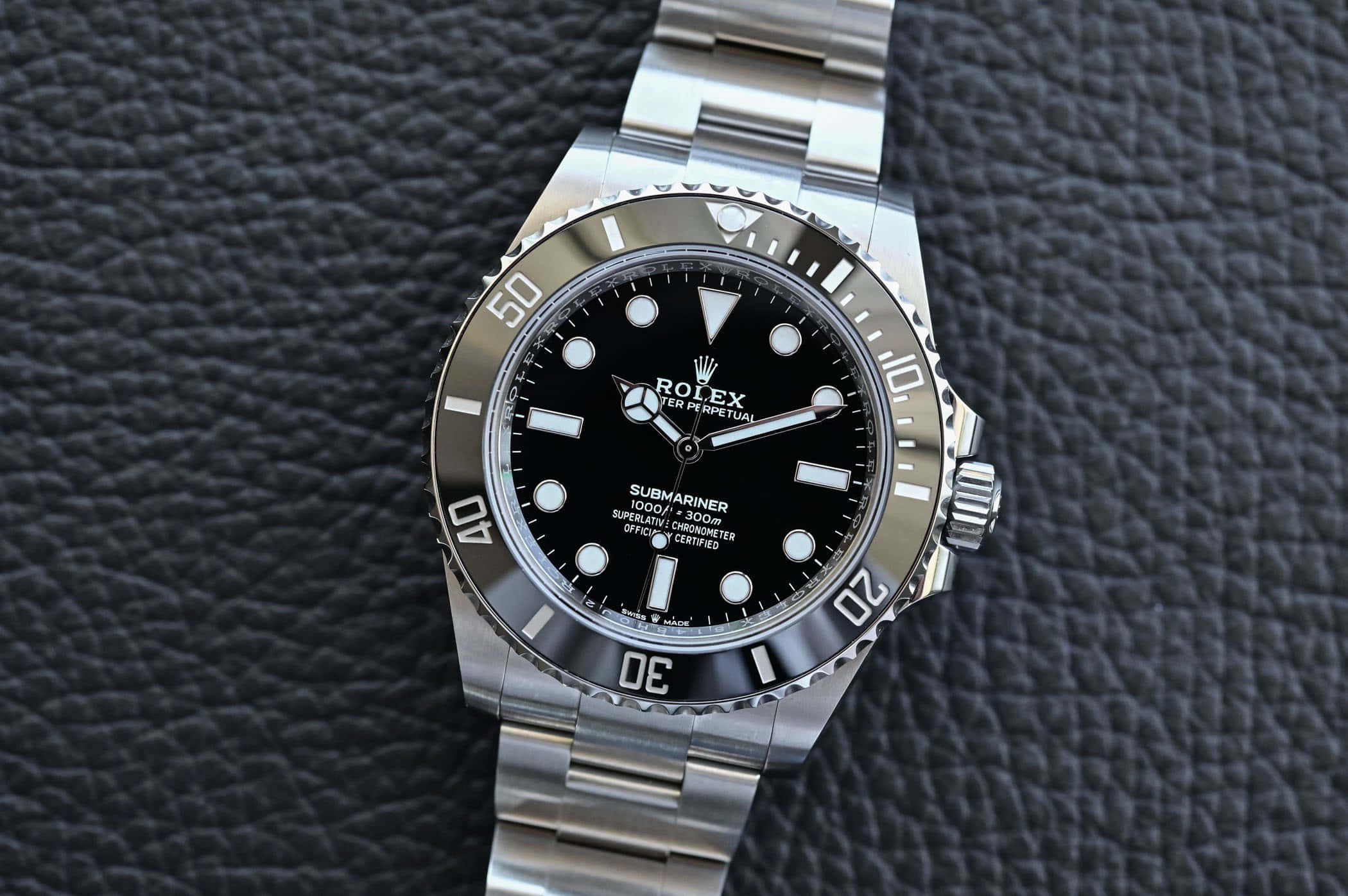 手錶 桌布 壁紙 — 一只時尚的不鏽鋼勞力士Submariner手錶，黑色錶盤，放置在帶紋理的黑色皮革上。