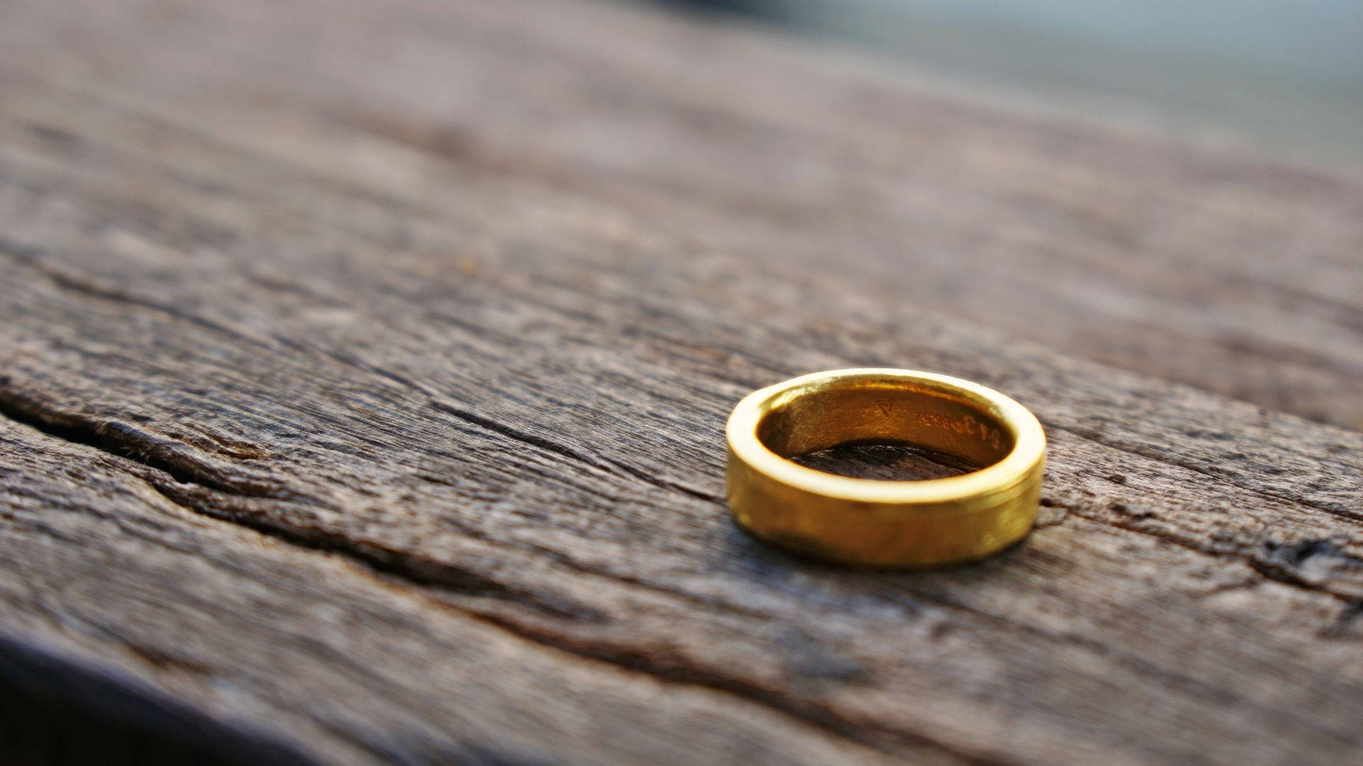 rings 桌布 壁紙 — 一只簡單的金戒指放在風化的木質表面上，帶有深紋理和自然質感。