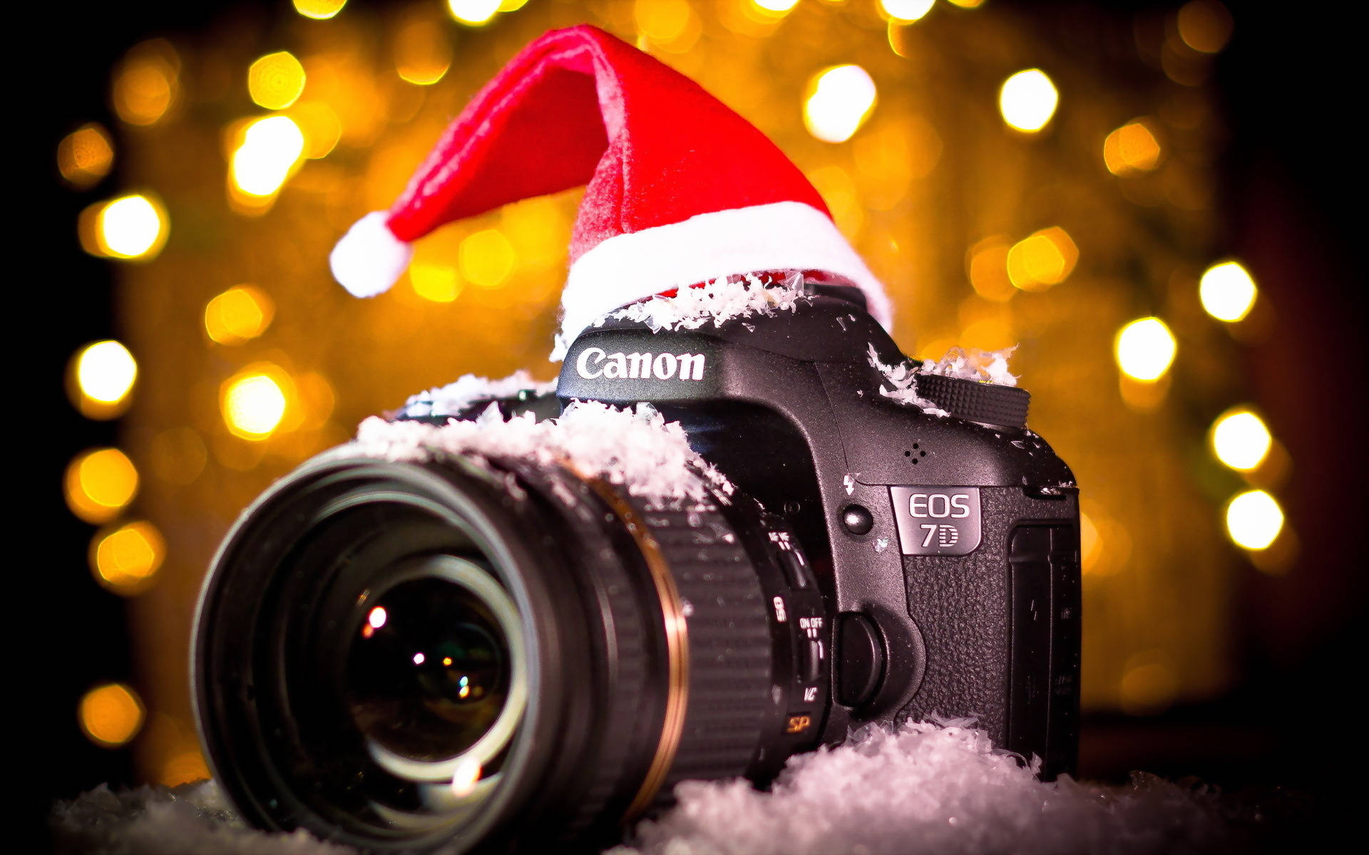 相機 桌布 壁紙 — 一台 Canon EOS 7D DSLR 相機，裝飾著紅色聖誕帽和假雪，置於溫暖的金色散景背景前。